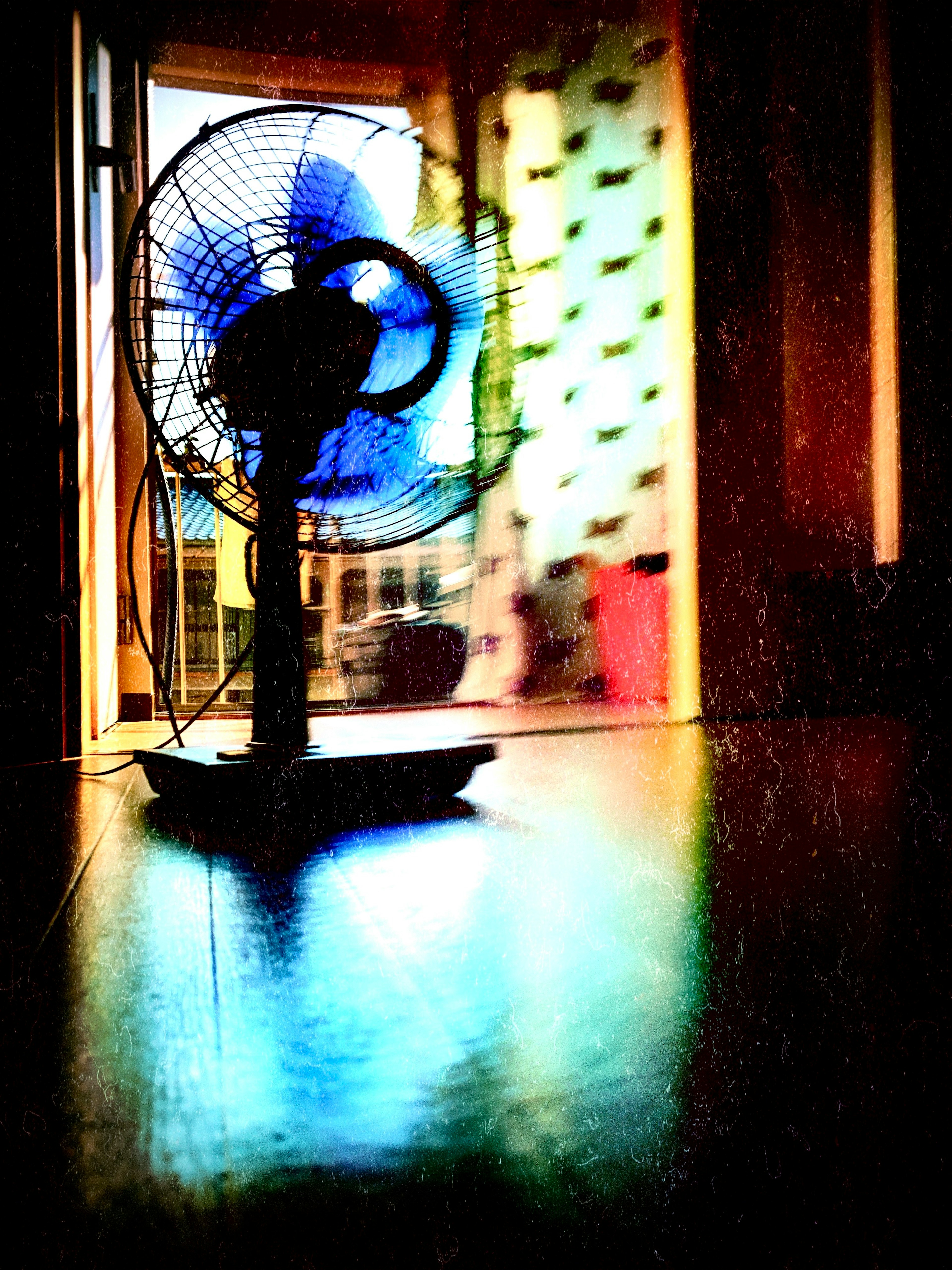 Scena interna con un ventilatore rotante dalle pale blu e riflessi sul pavimento