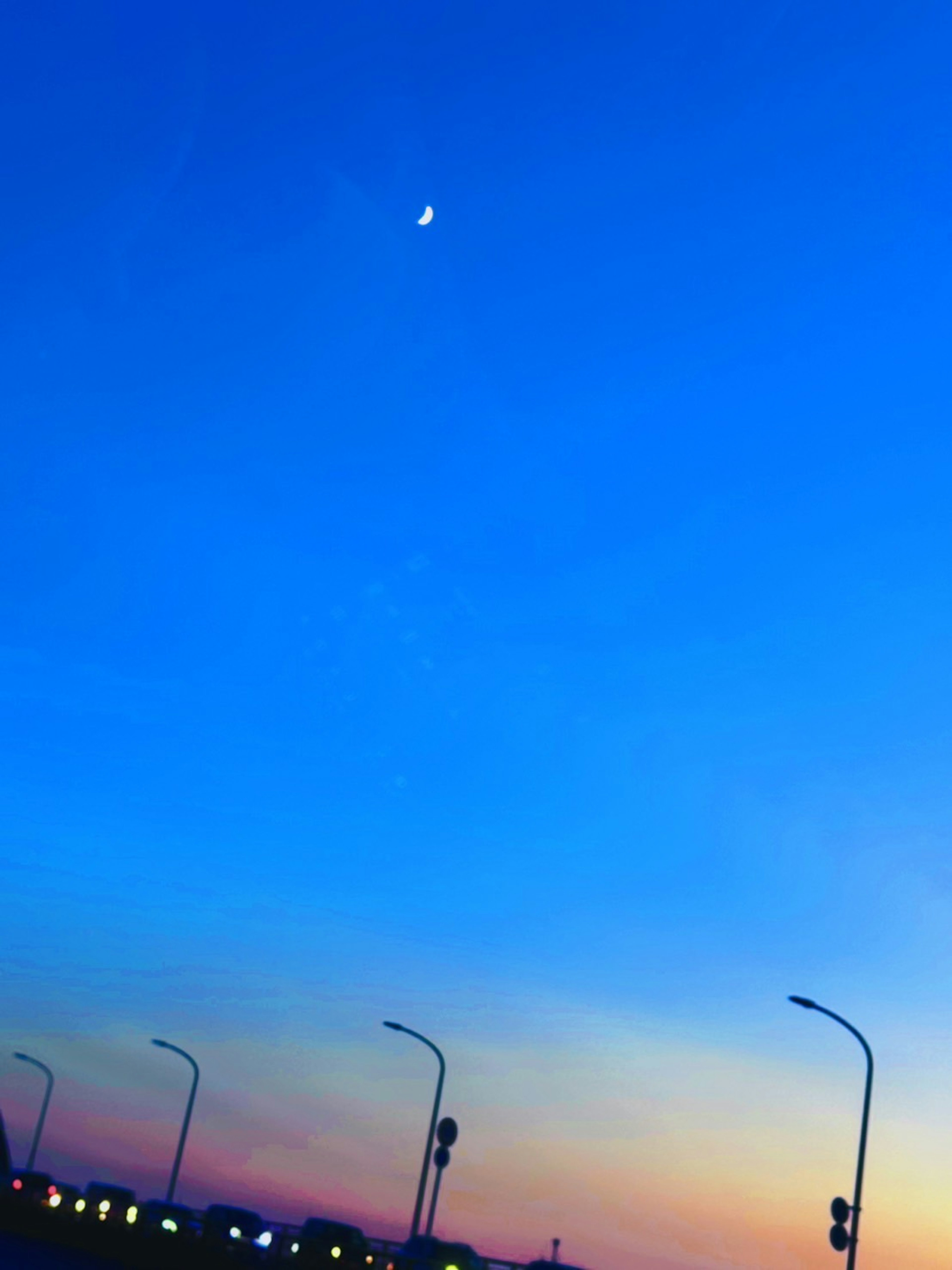 Une lune croissante dans un ciel bleu avec un coucher de soleil coloré