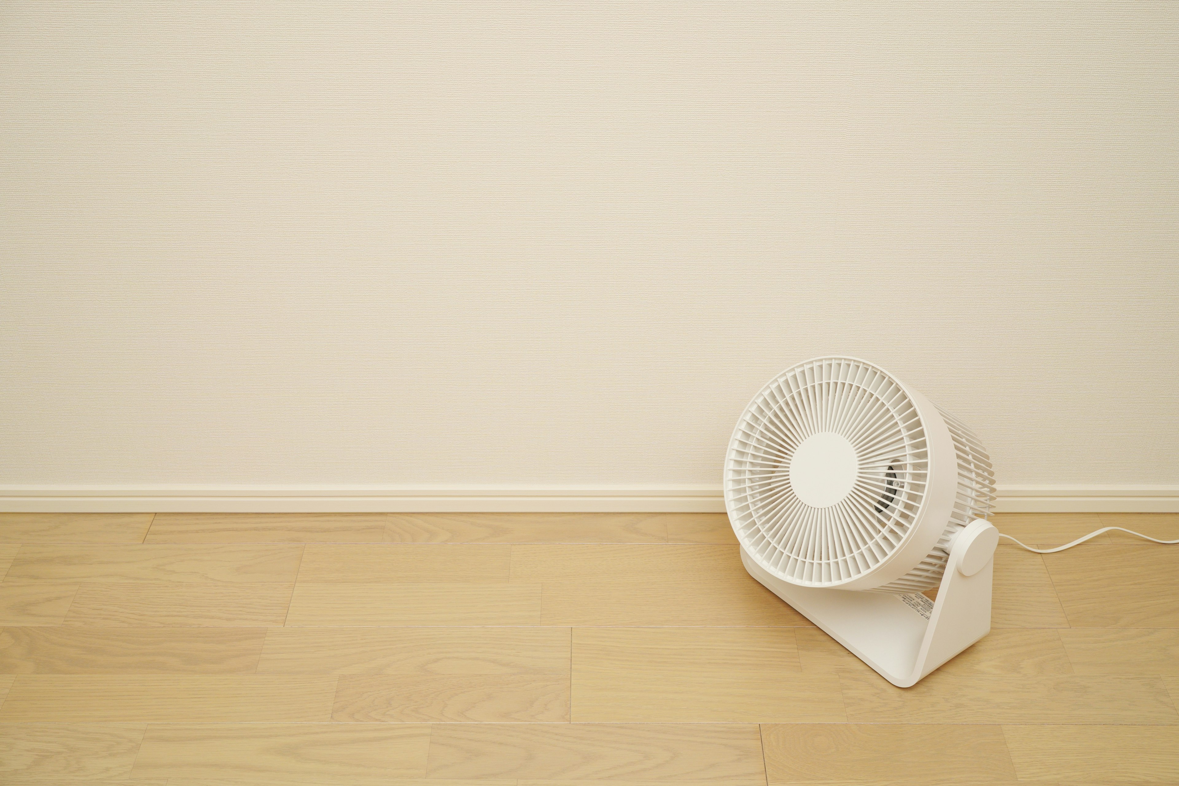 Un ventilador blanco apoyado contra una pared en un entorno interior simple