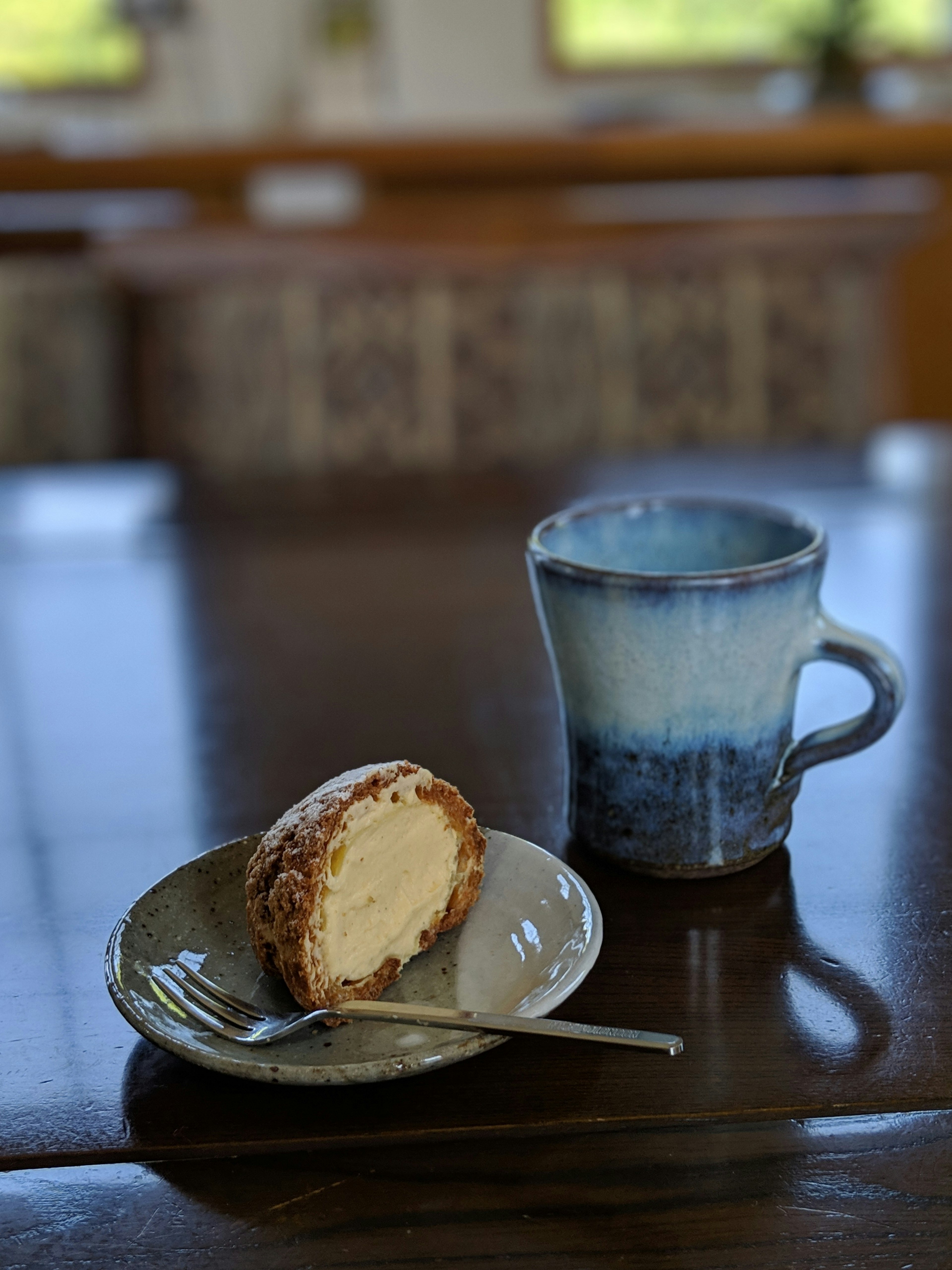 Cream-filled dessert on a plate with a blue mug on a wooden table