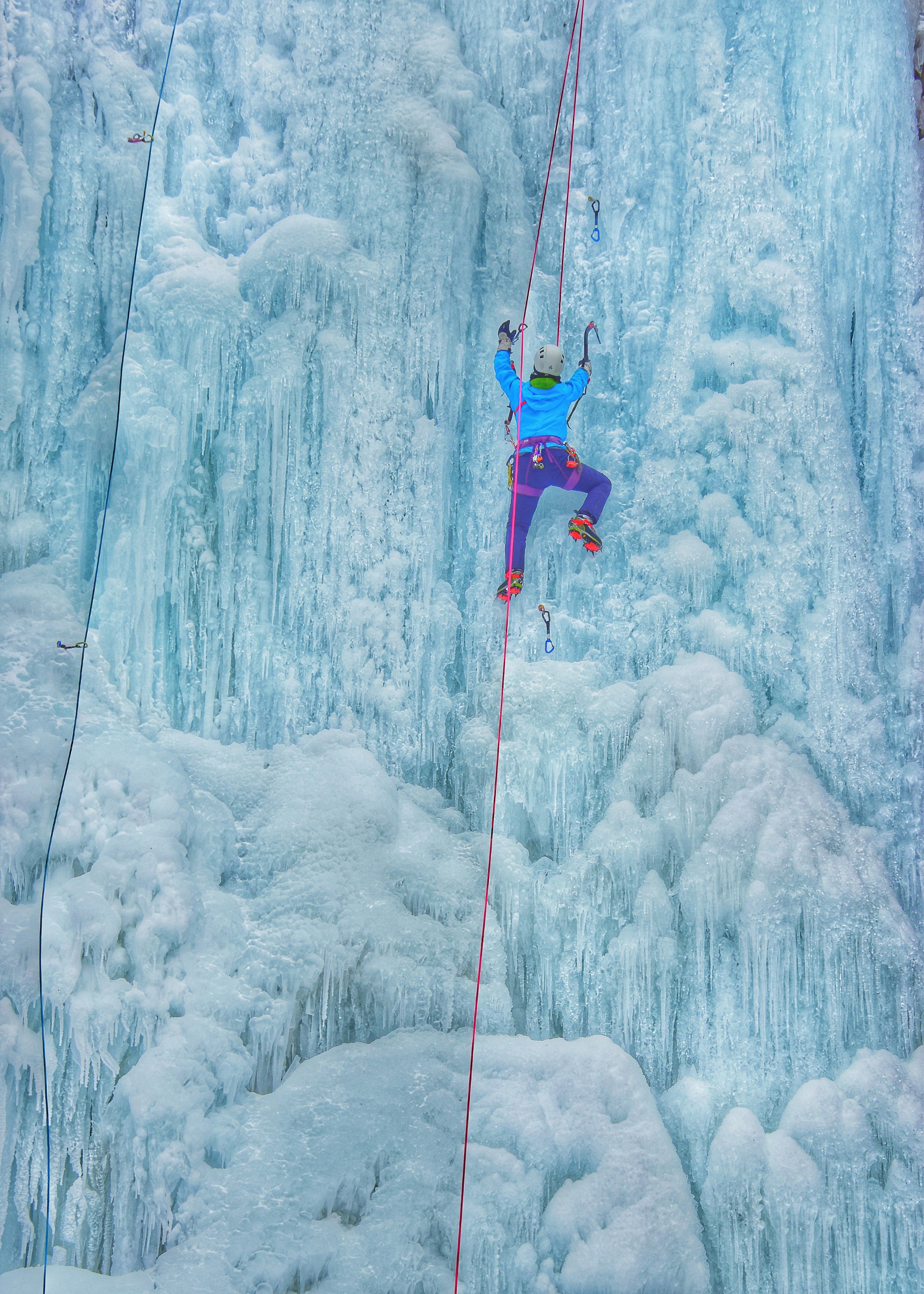 Escalador con traje azul y pantalones morados subiendo una pared de hielo