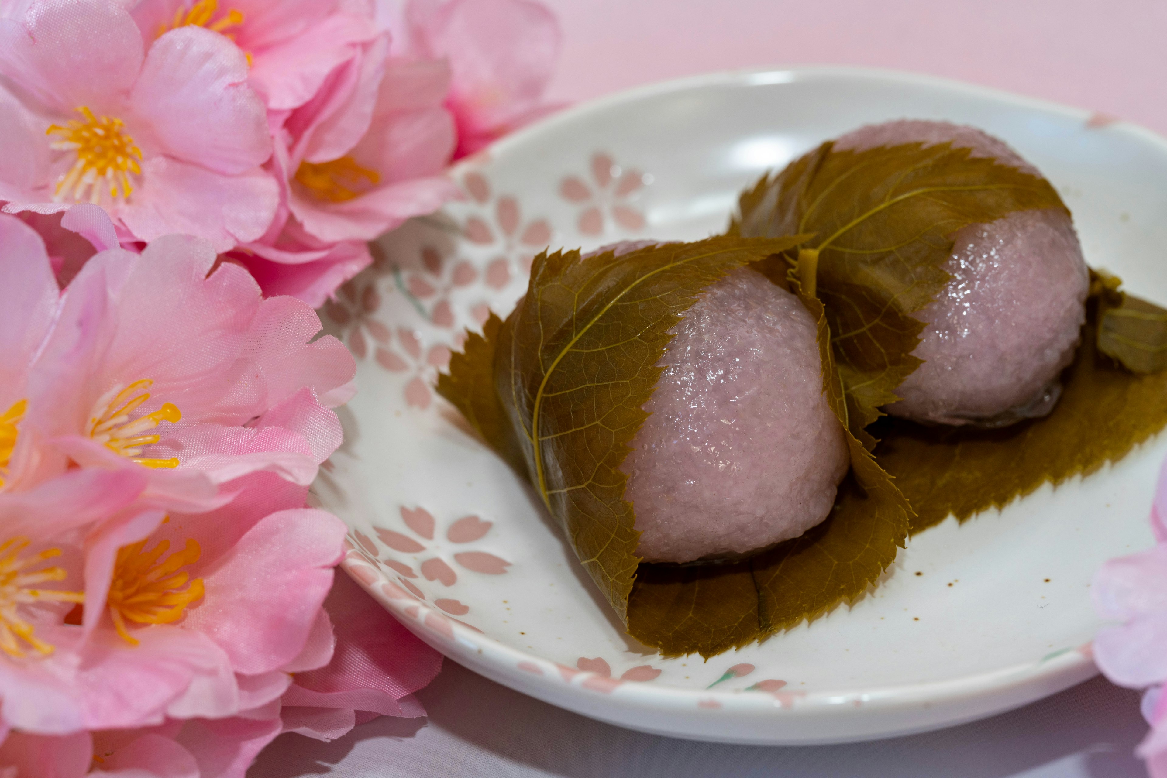 Plate of sakura mochi next to cherry blossom petals