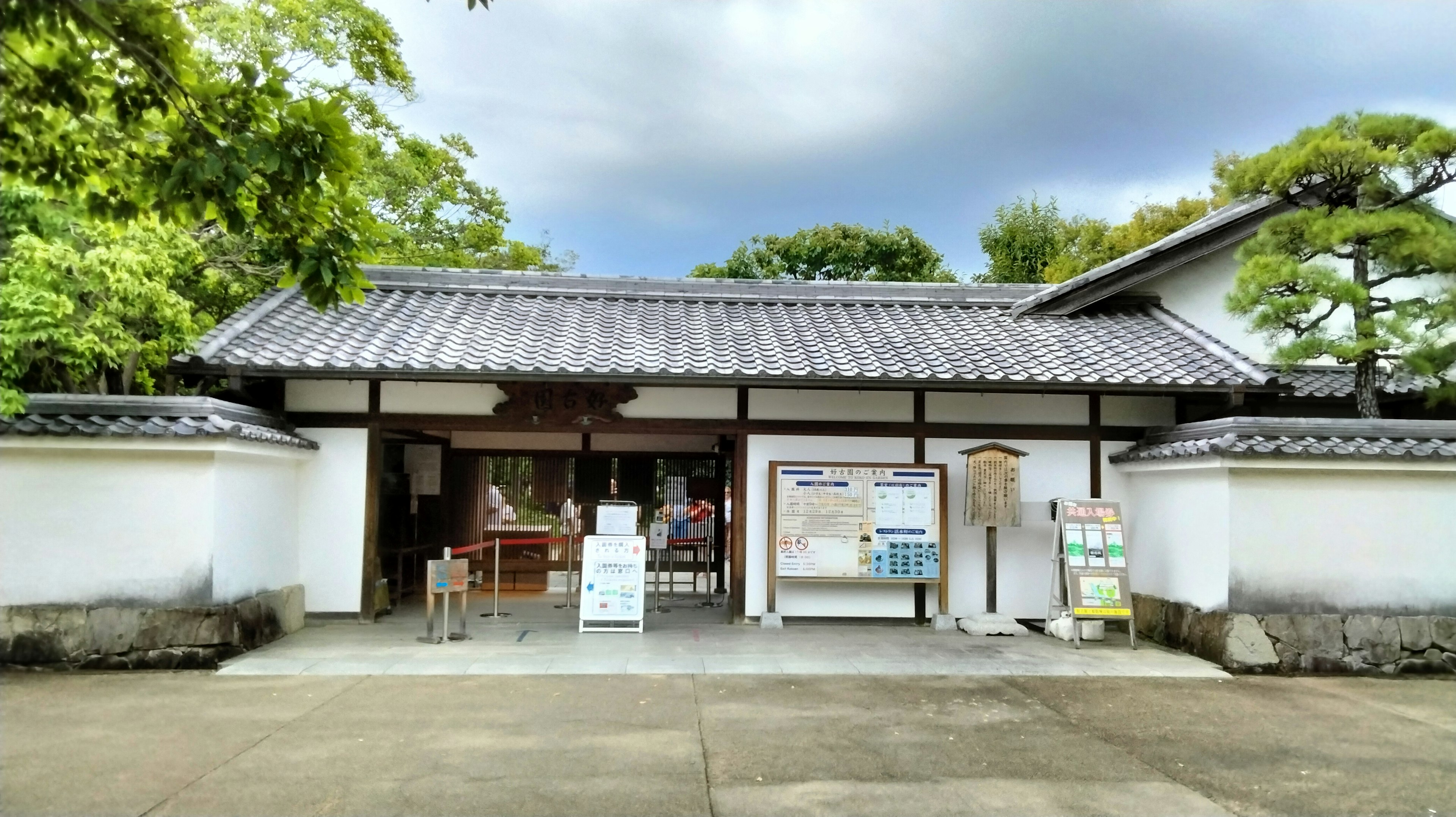 Außenansicht eines traditionellen japanischen Gebäudes mit grünen Bäumen und grauem Himmel