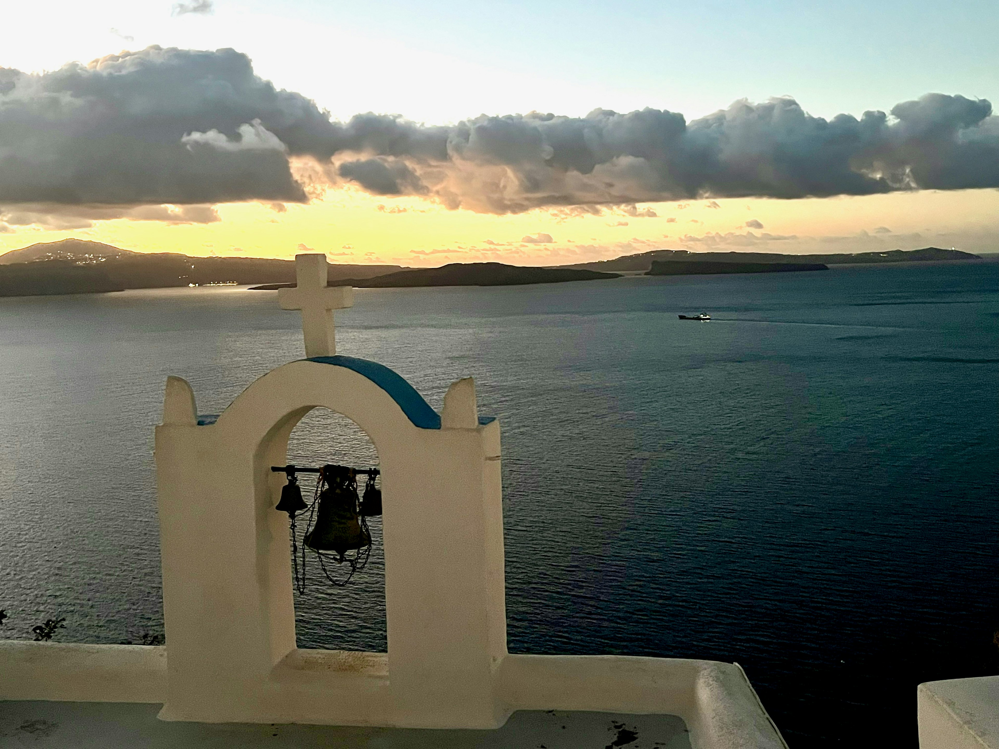 Torre di chiesa bianca con cupola blu e campane che sovrasta il mare al tramonto