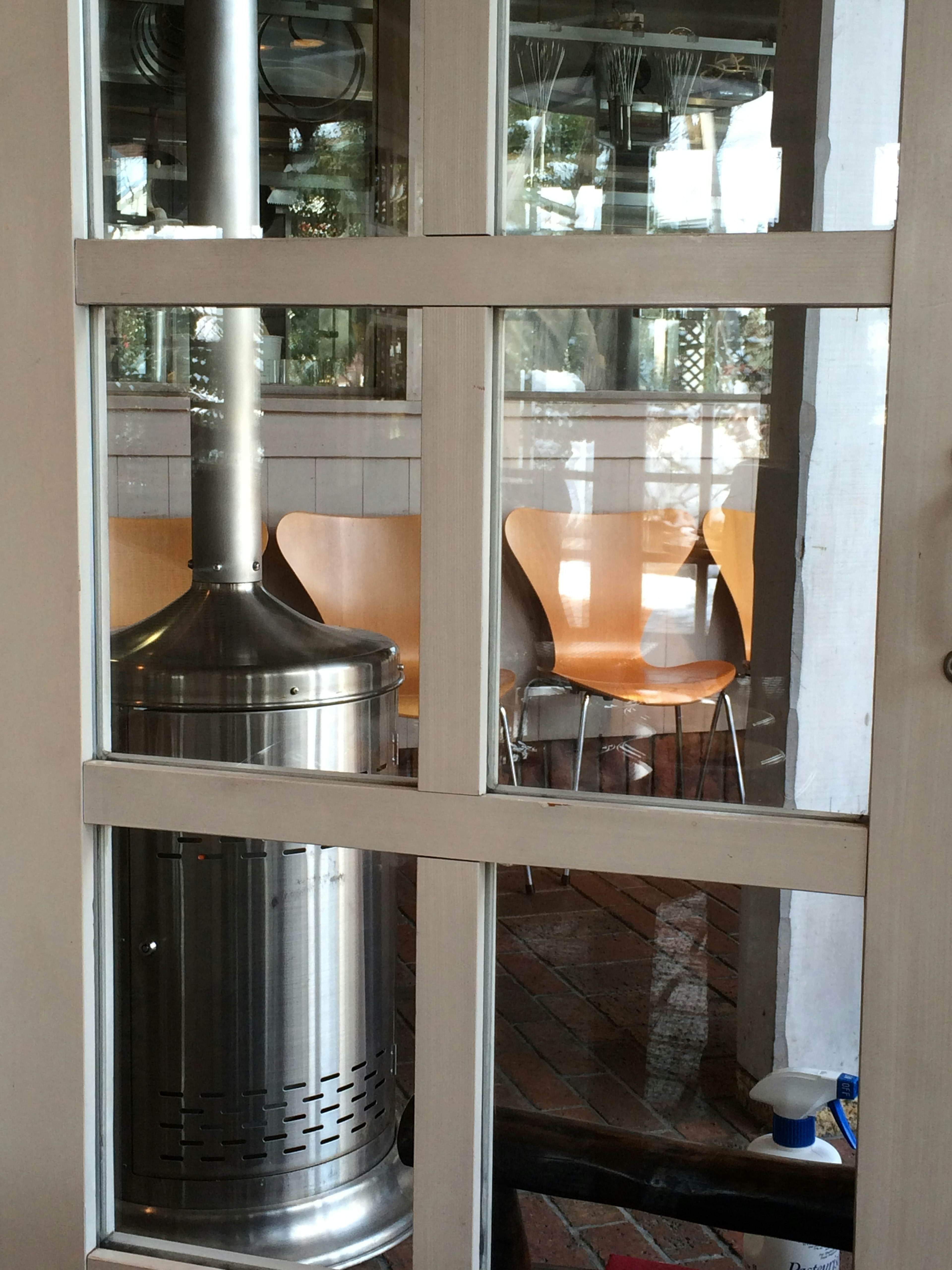 Metal outdoor heater visible through a glass door with empty chairs