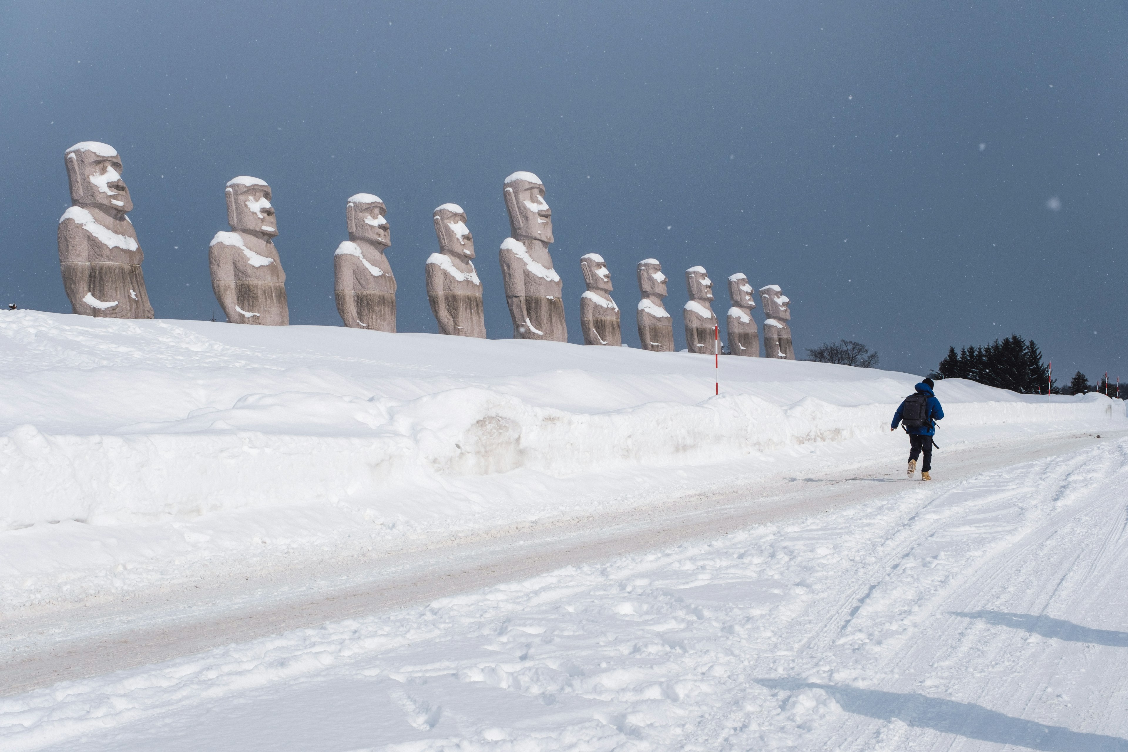 Un paisaje nevado con estatuas Moai alineadas y una persona caminando