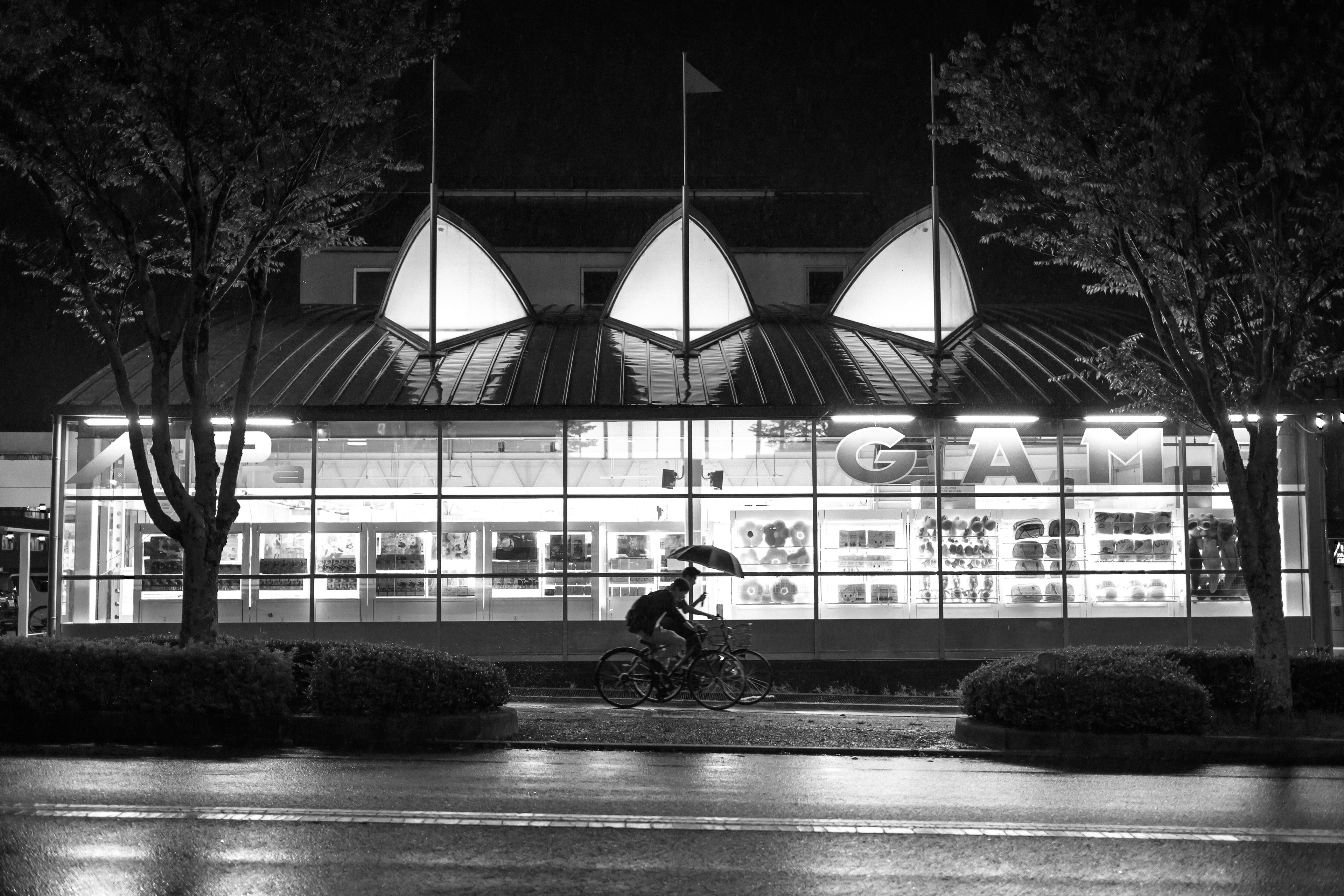 Una persona en bicicleta con un paraguas de noche frente a un edificio iluminado