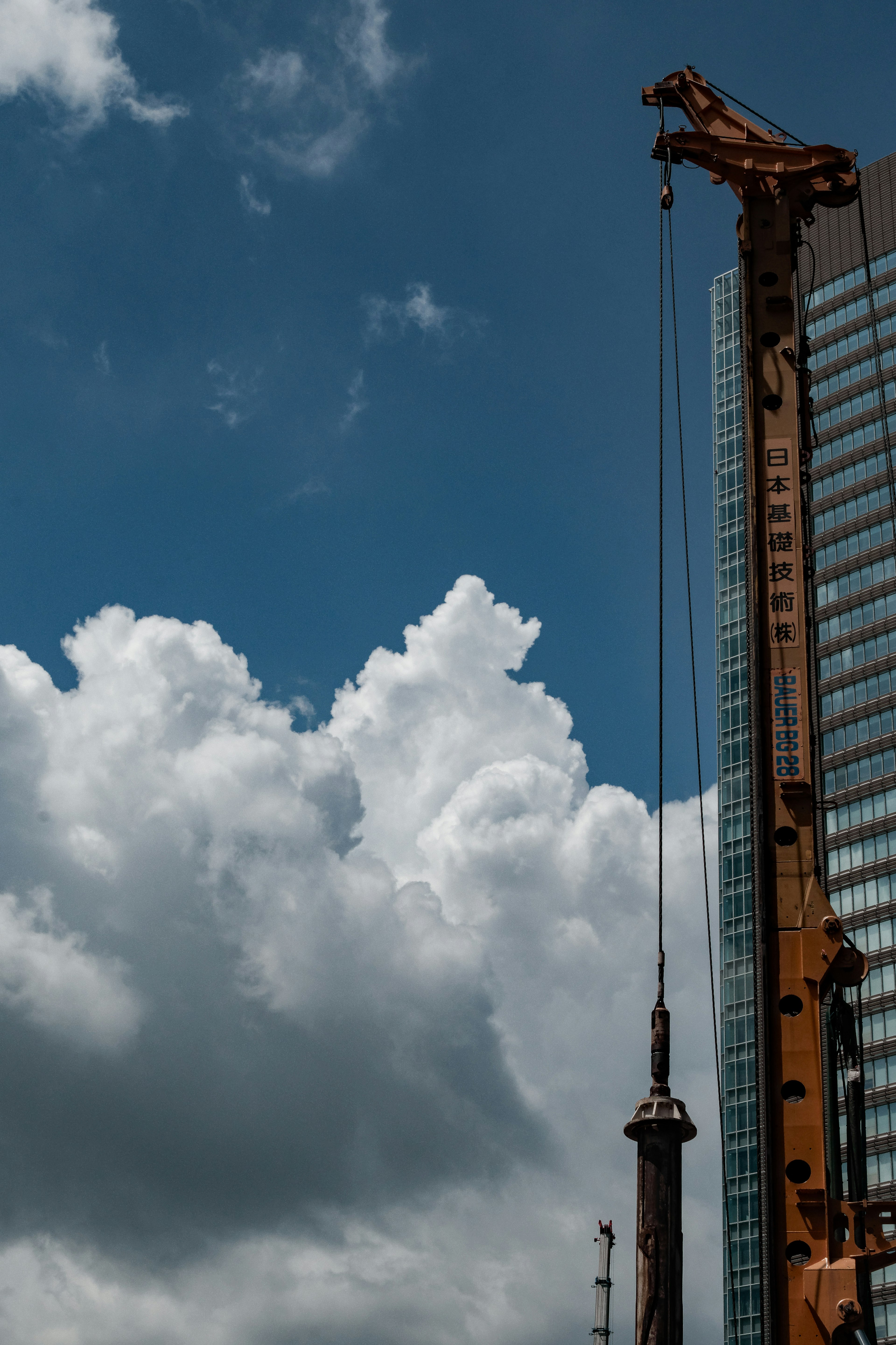 Grúa junto a un rascacielos bajo un cielo azul con nubes