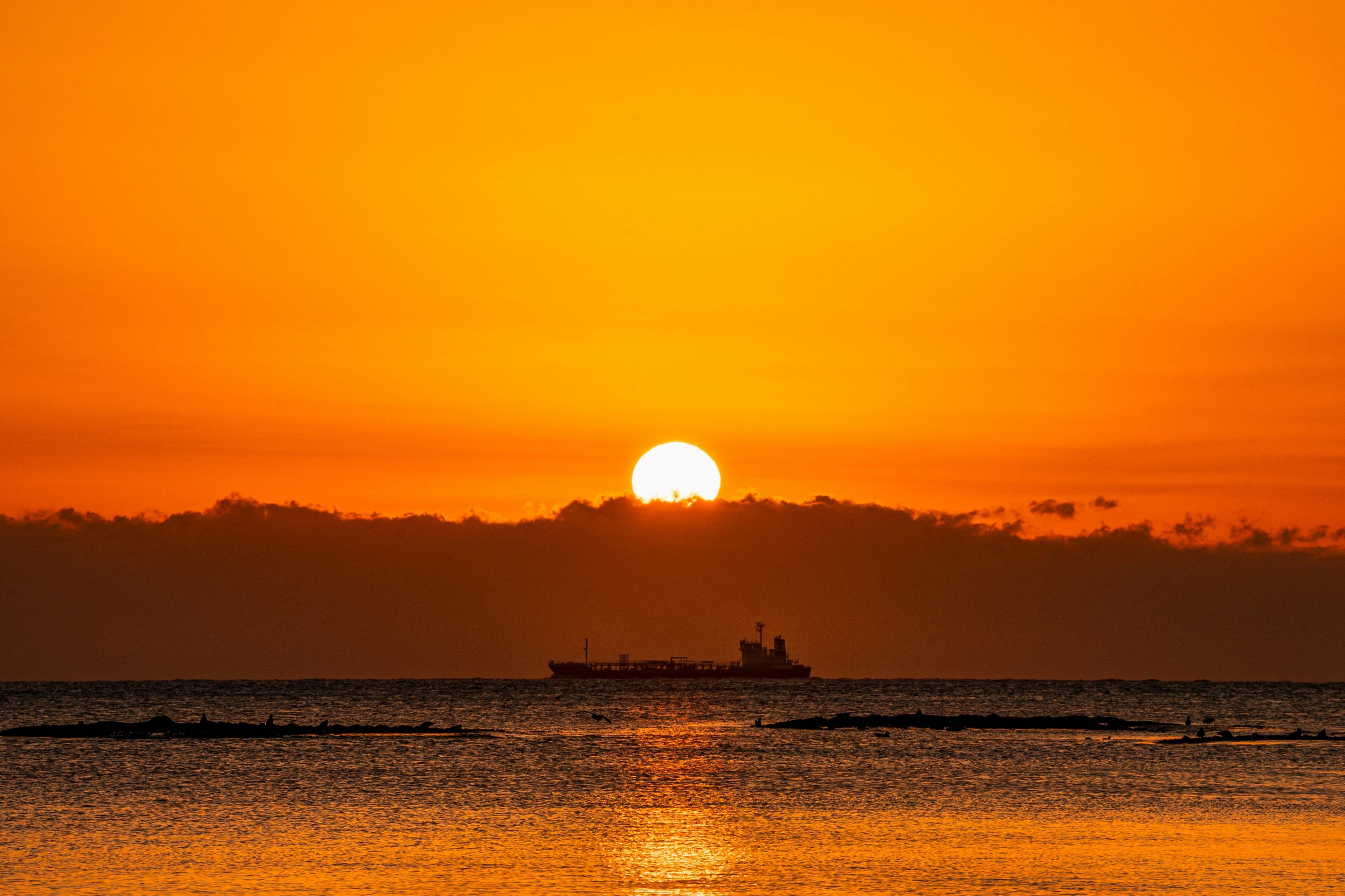 オレンジ色の空に沈む太陽と海に浮かぶ船