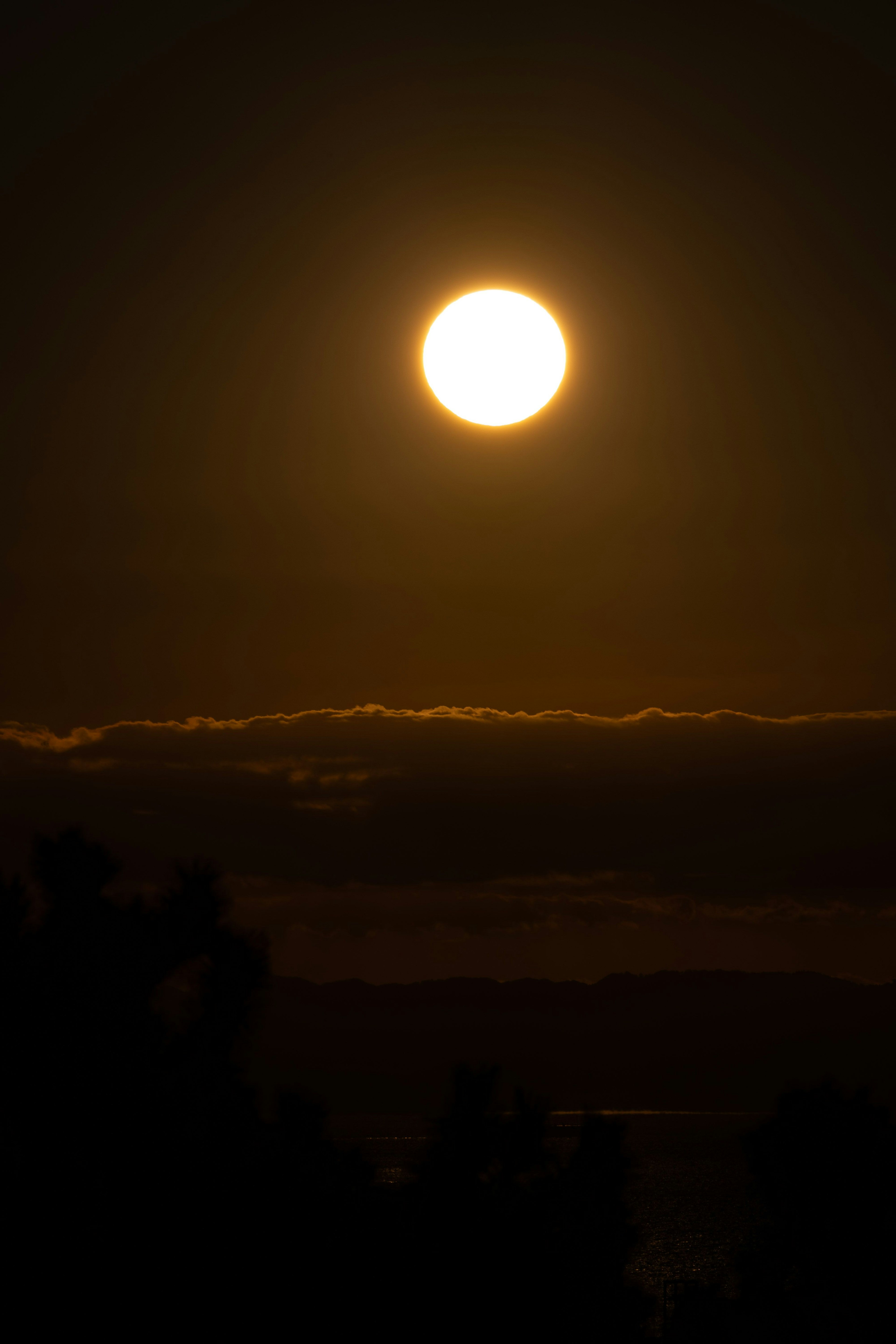 夕暮れの空に浮かぶ大きな太陽と雲のシルエット