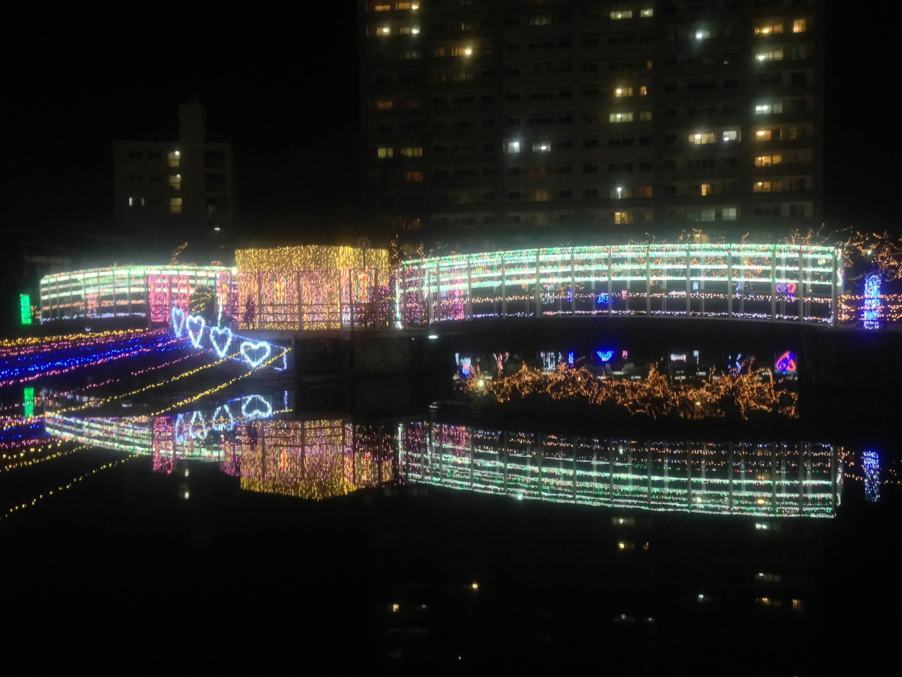 Colorful lights reflecting on the river at night with heart-shaped decorations on the bridge