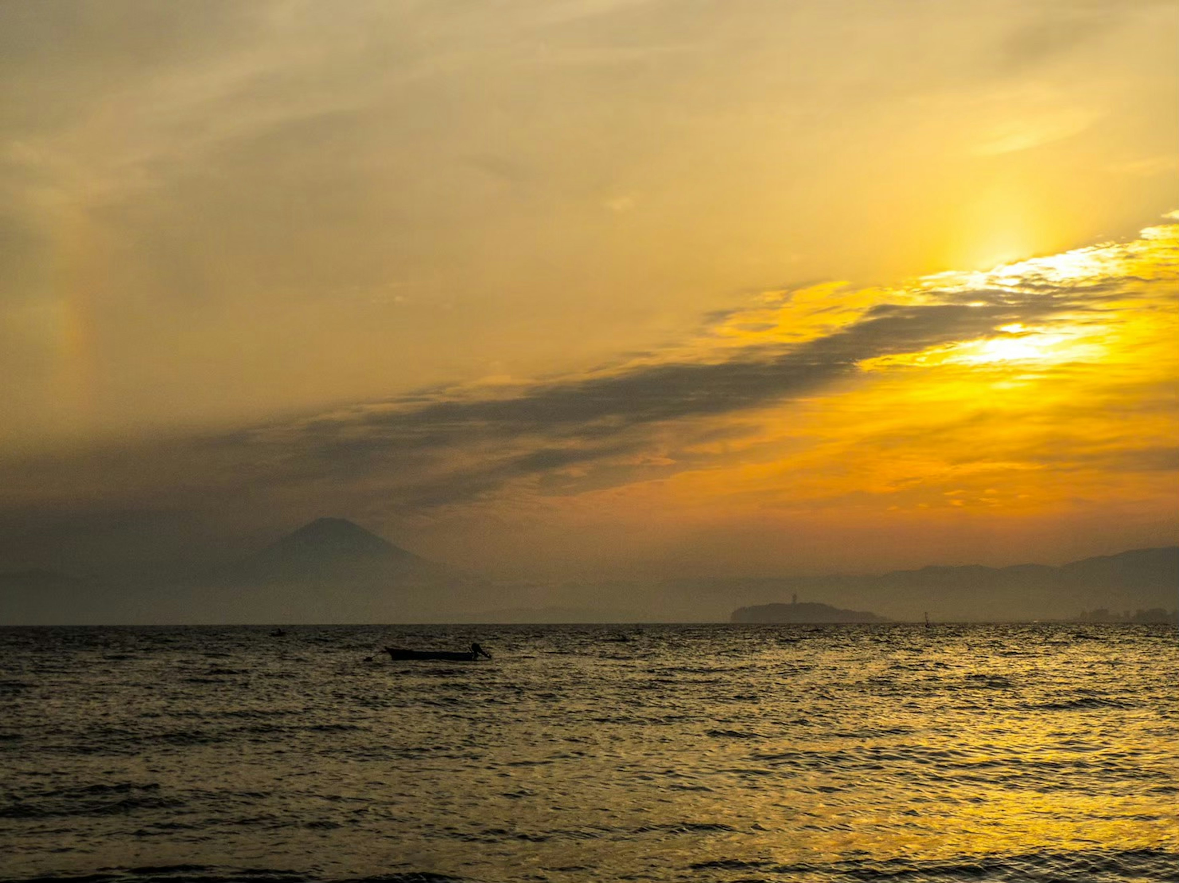 Siluet gunung dan perahu kecil di laut saat matahari terbenam