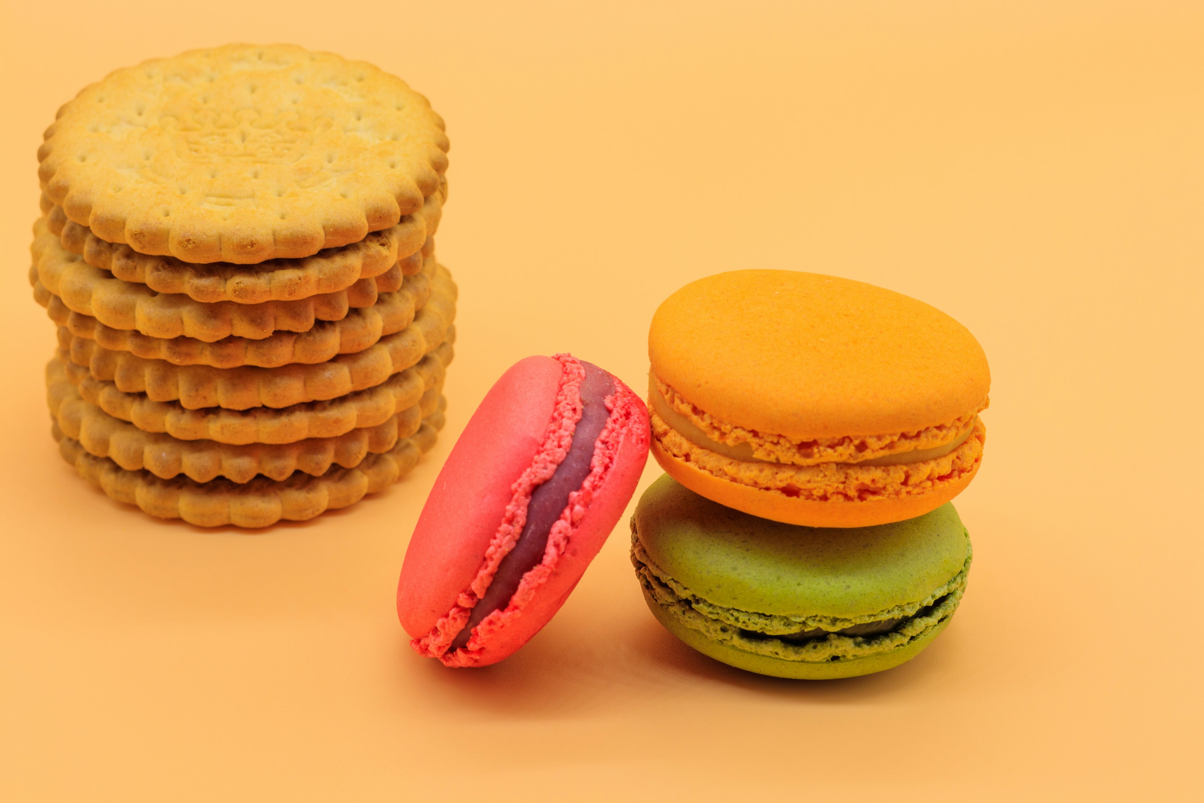 Macaron berwarna-warni dan biskuit di latar belakang pastel tiga macaron cerah ditumpuk bersama