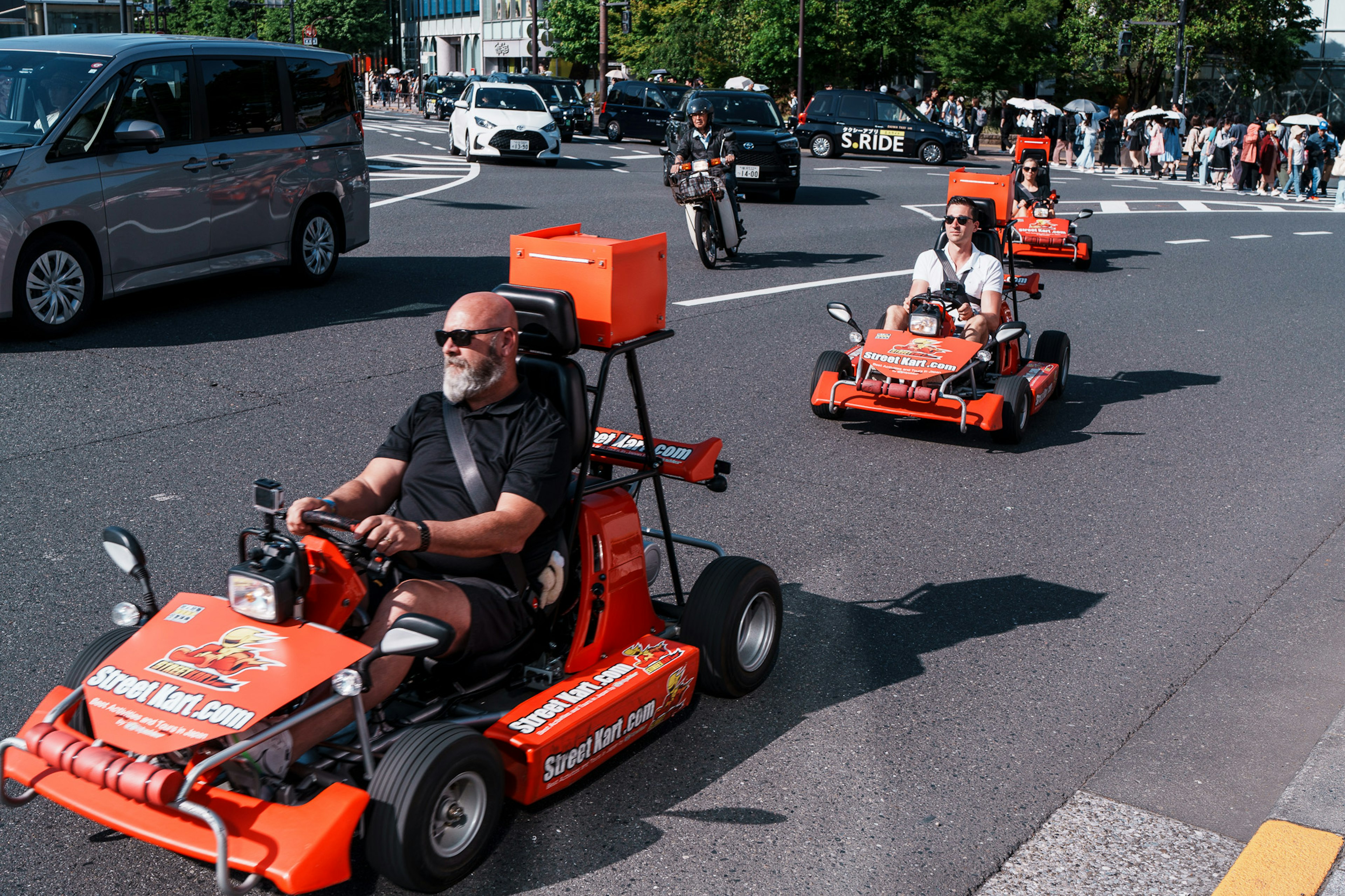 オレンジ色のミニカートに乗る男性たちが都市の道路を走っている