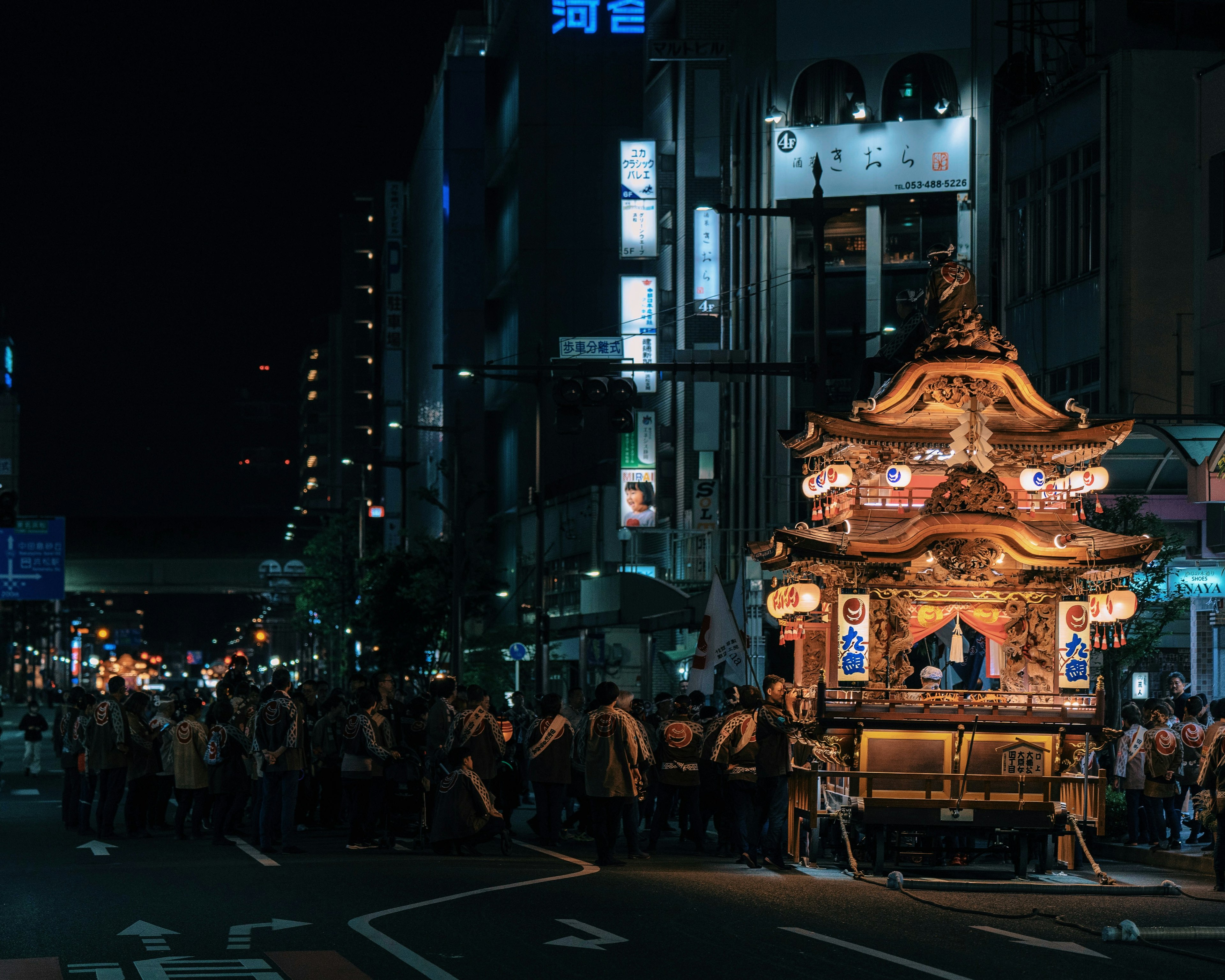 Night festival scene with a brightly lit float and procession in the street