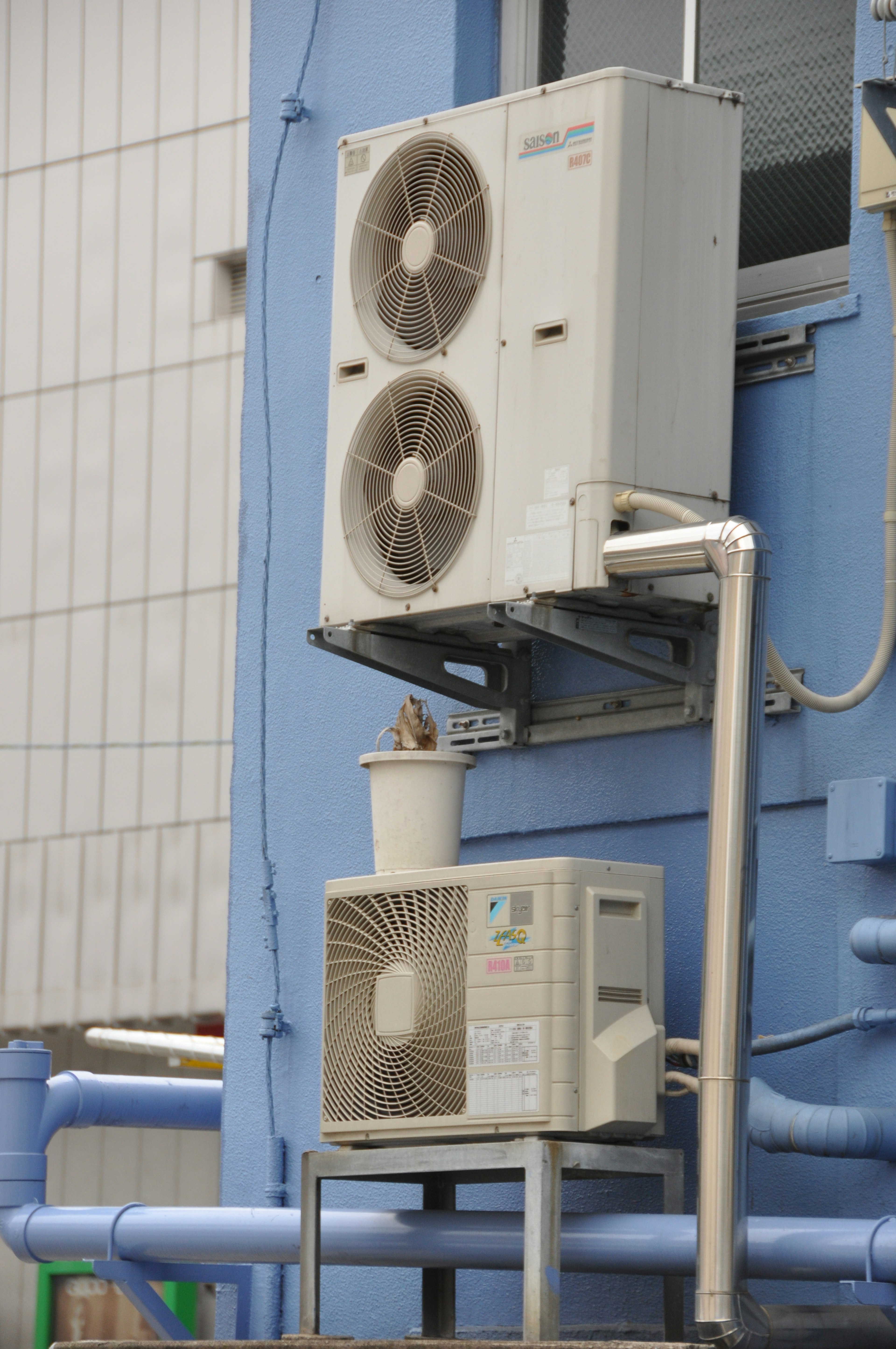 Two air conditioning units mounted on a blue wall with visible piping