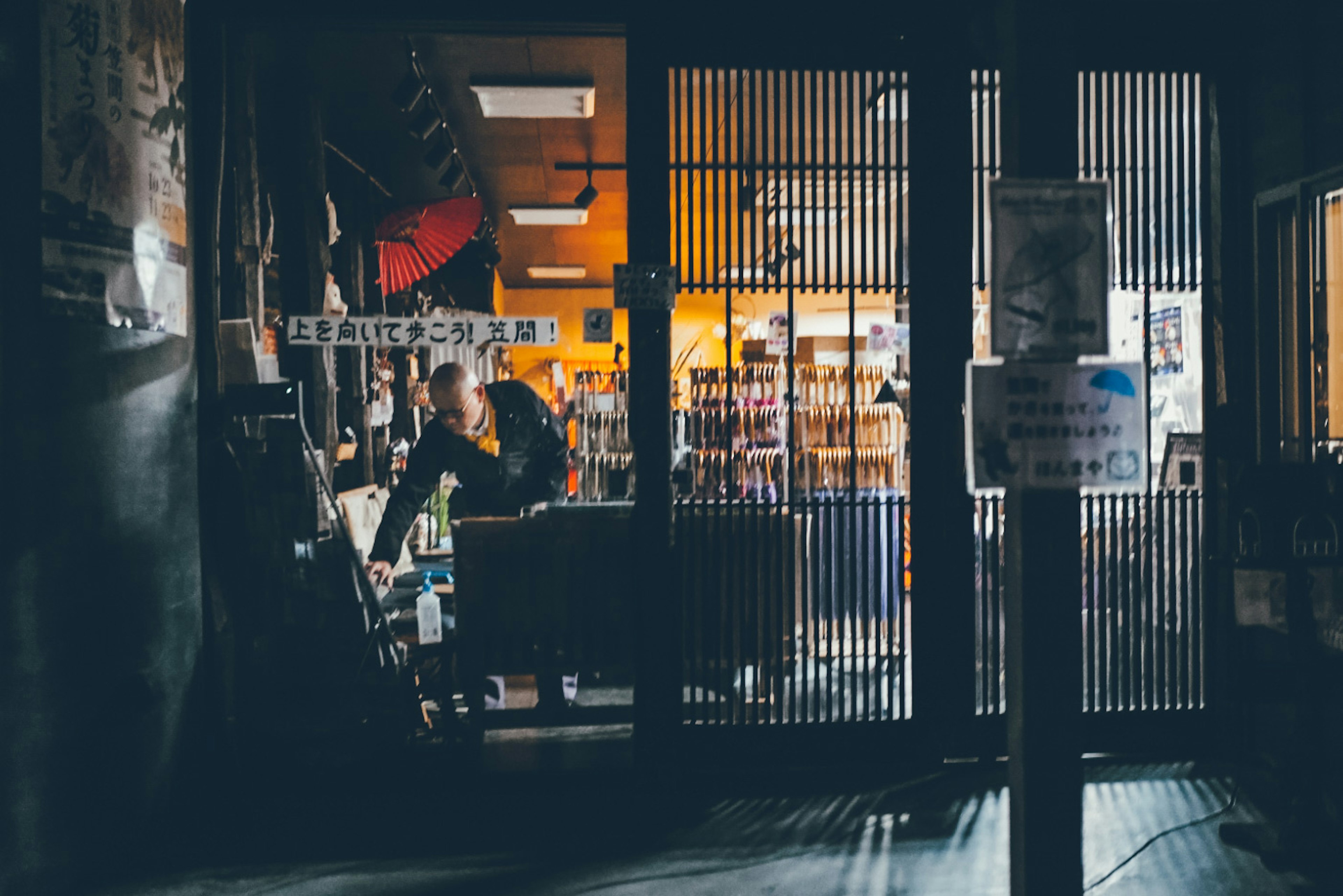 店内の明かりが灯る書店の外観、人物がカウンターで作業中