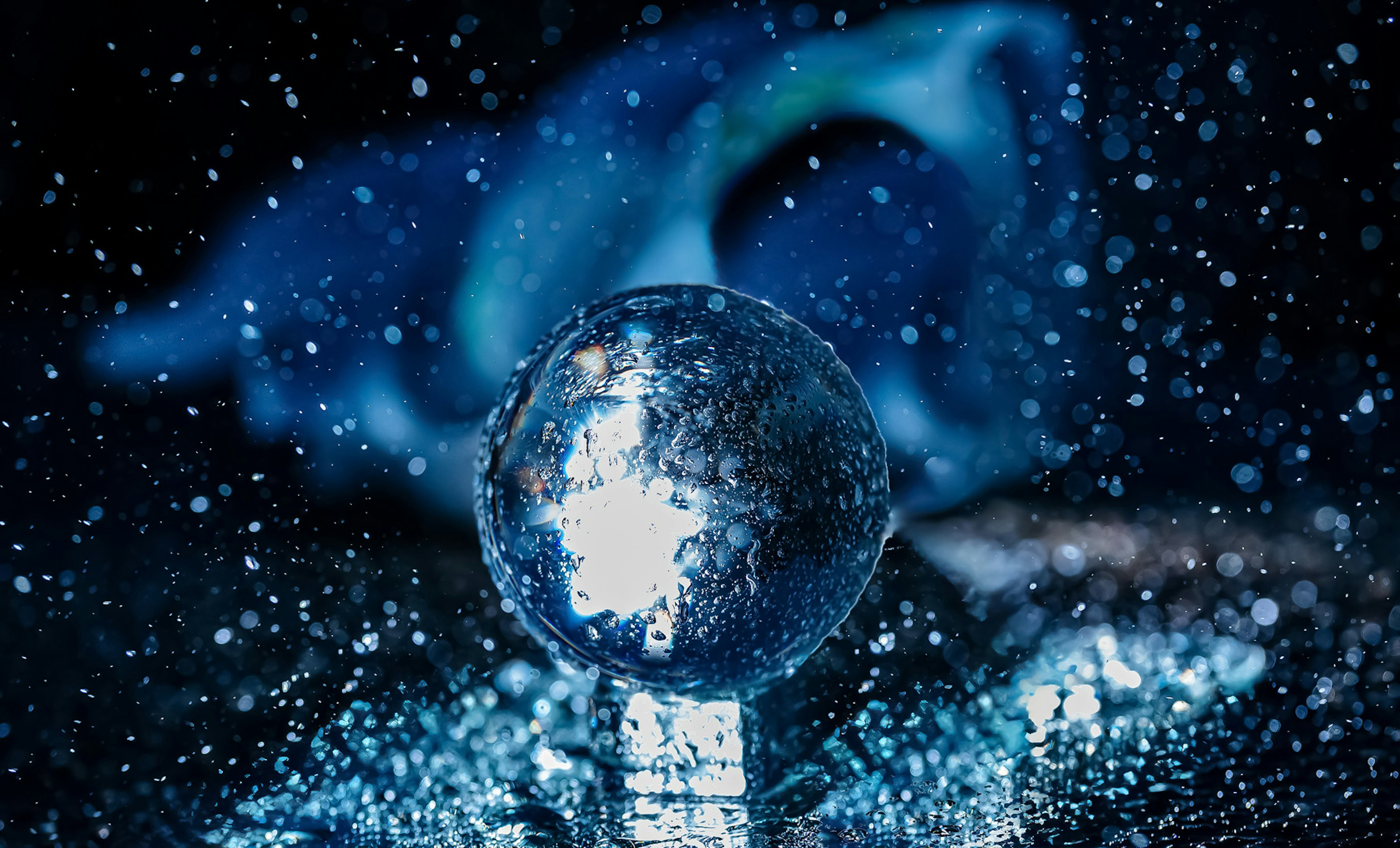 A transparent sphere shining amidst splashes of water against a blue background