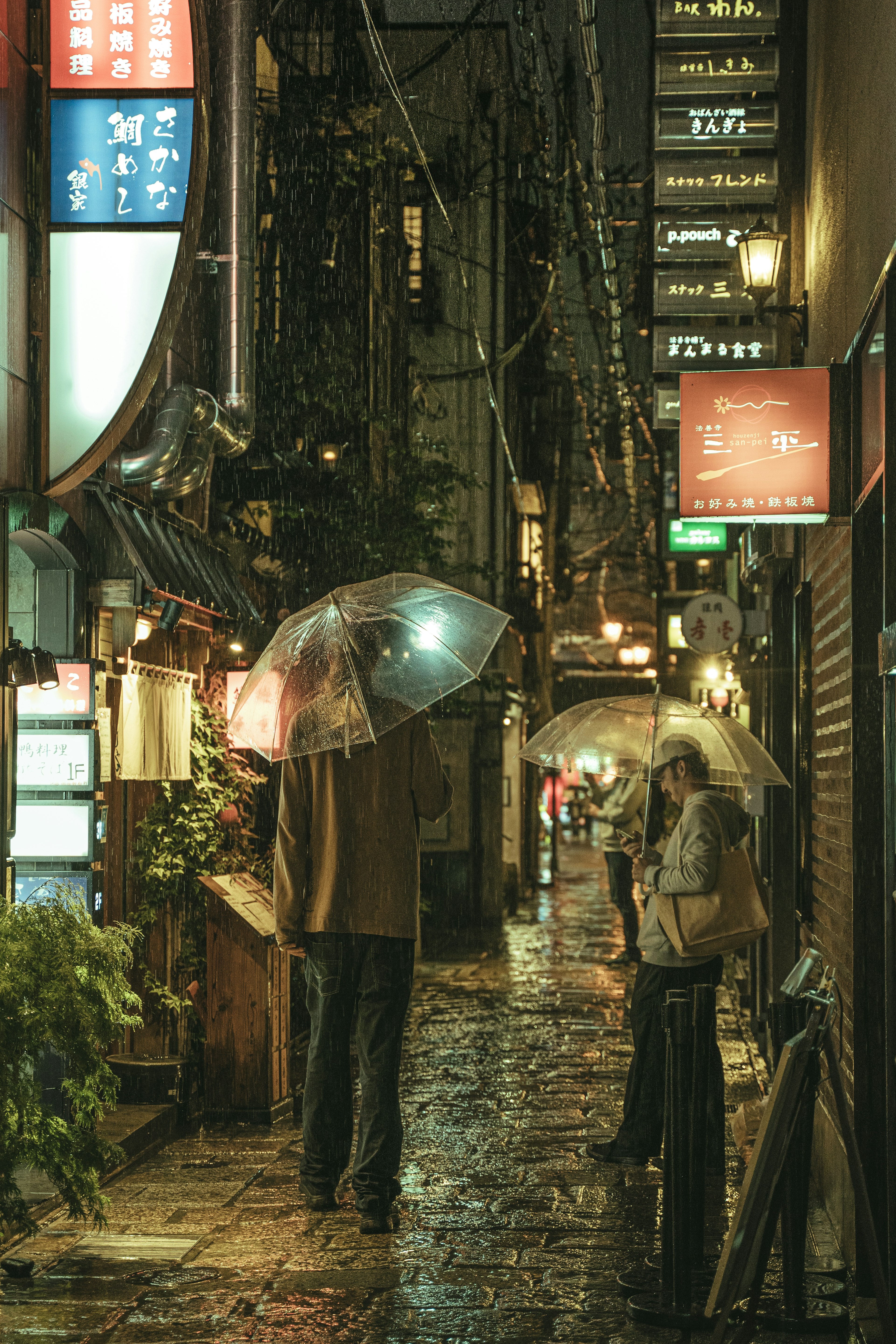 Personas con paraguas en un callejón estrecho bajo la lluvia con letreros de tiendas