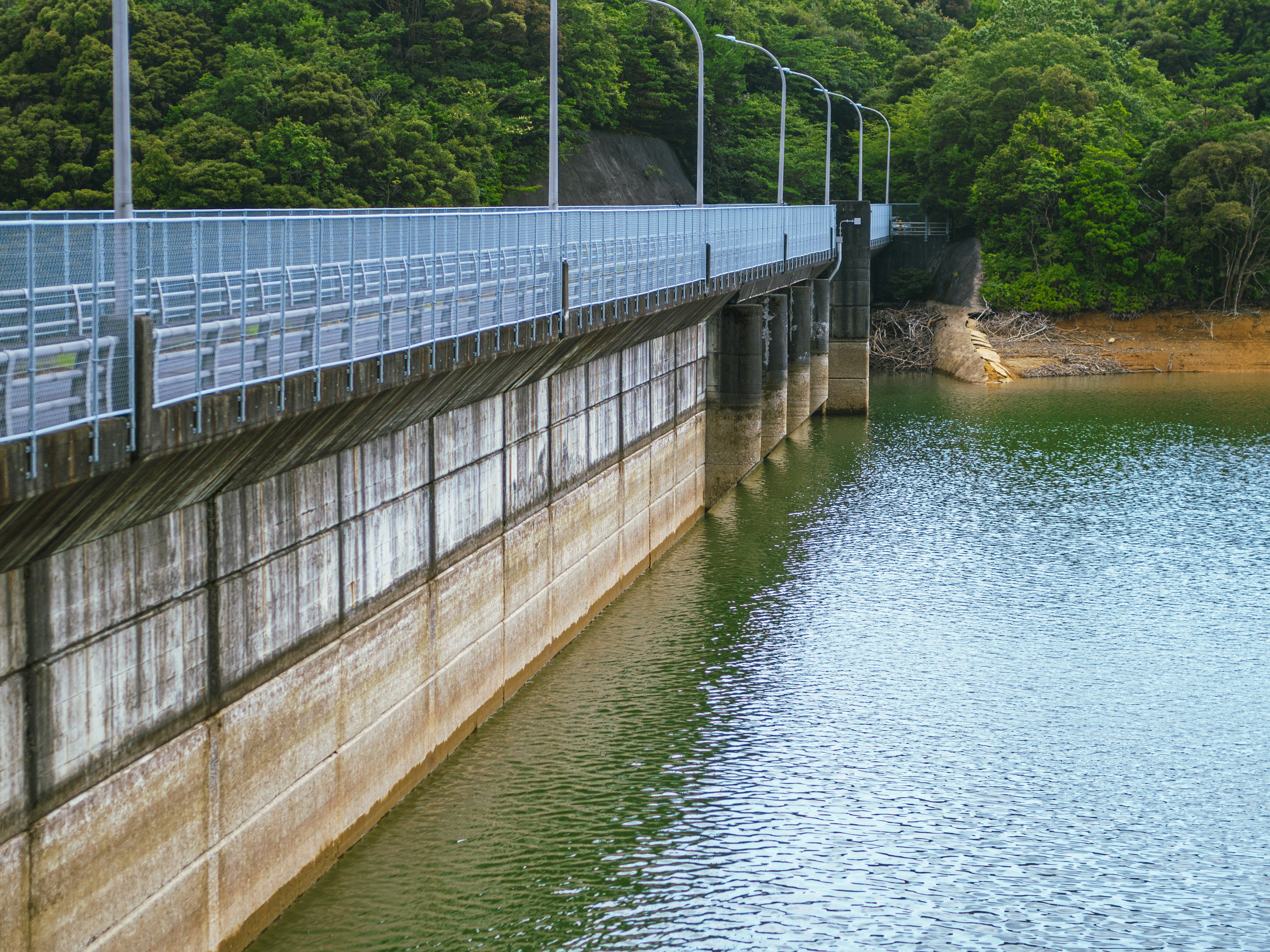 Concrete dam wall with a view of green trees and water