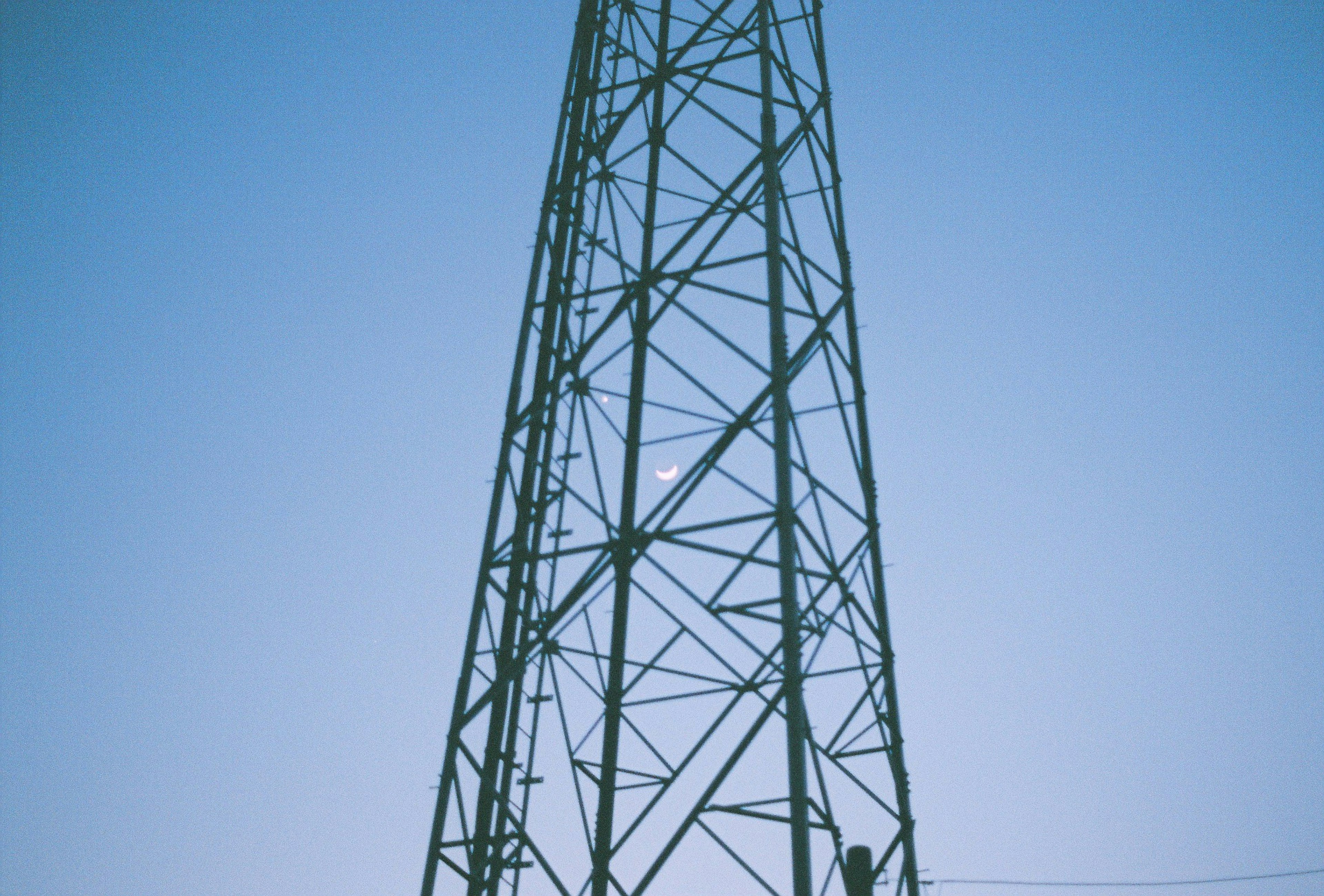 Menara logam tinggi di bawah langit biru dengan bulan kecil