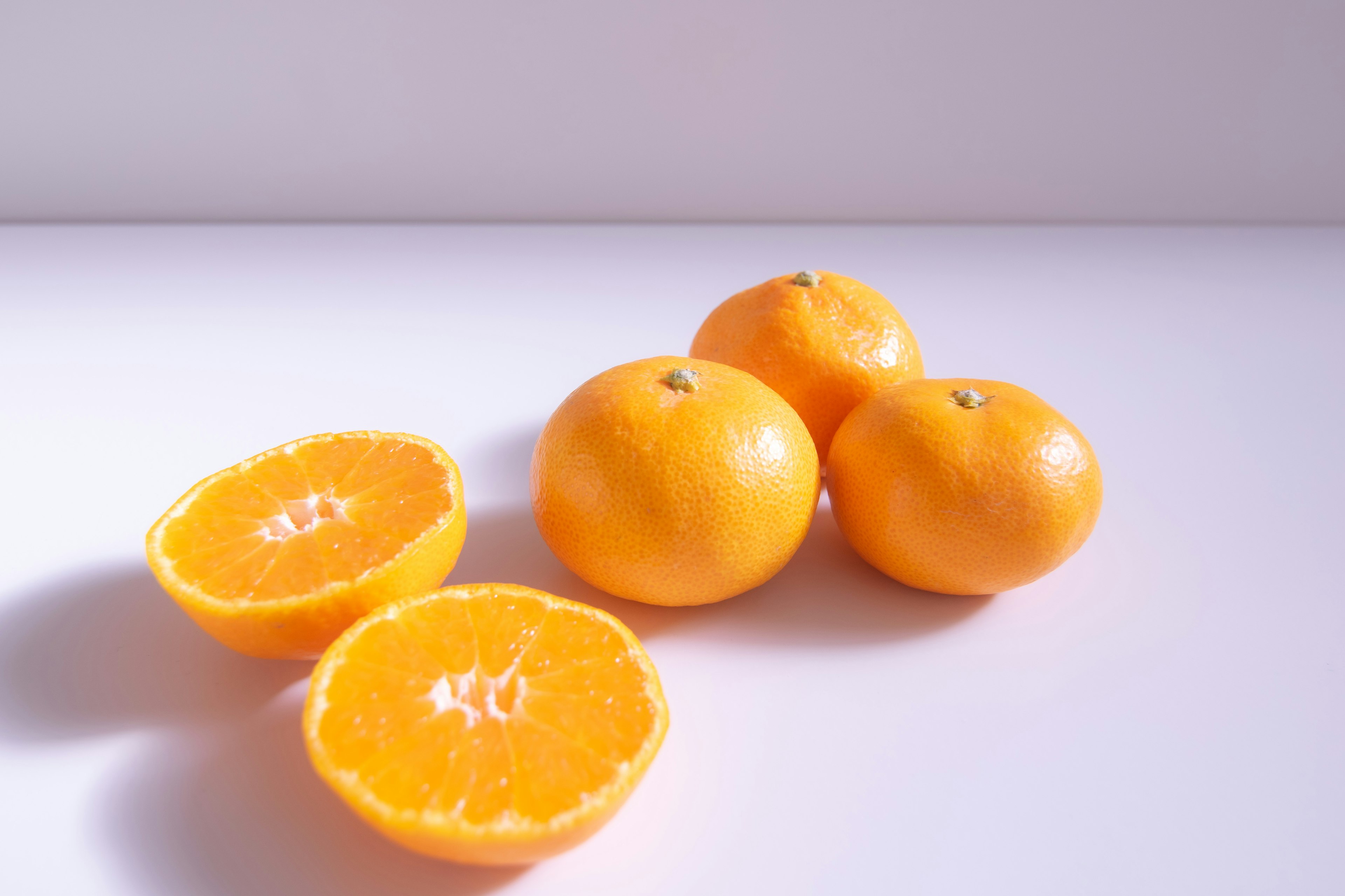 Quatre oranges brillantes et deux moitiés d'orange sur un fond clair