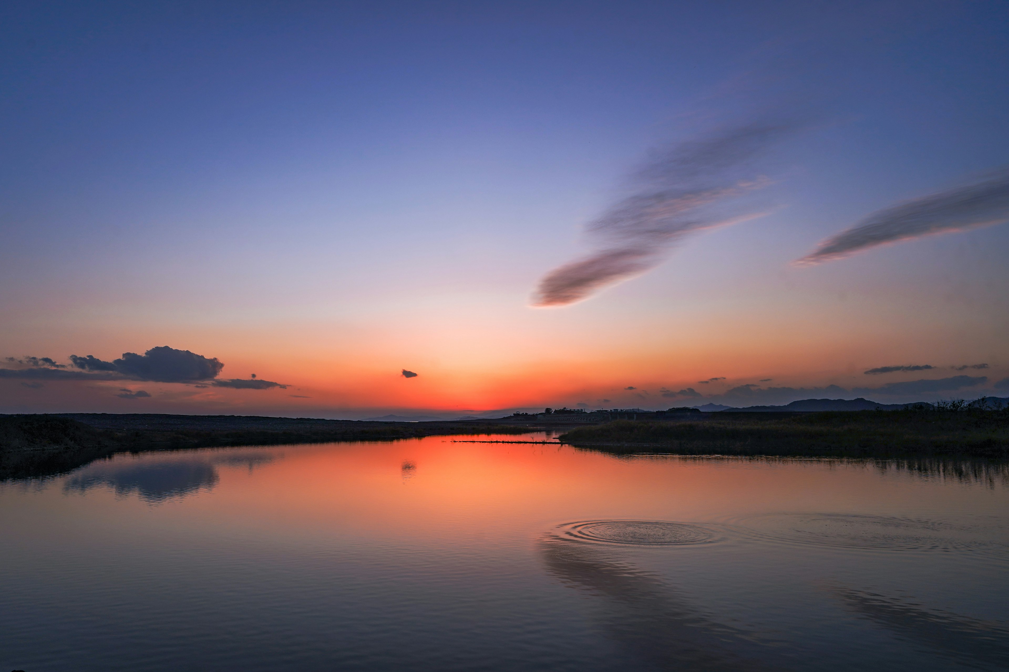 静かな川のほとりでの夕焼けの風景 水面に映るオレンジと青のグラデーション