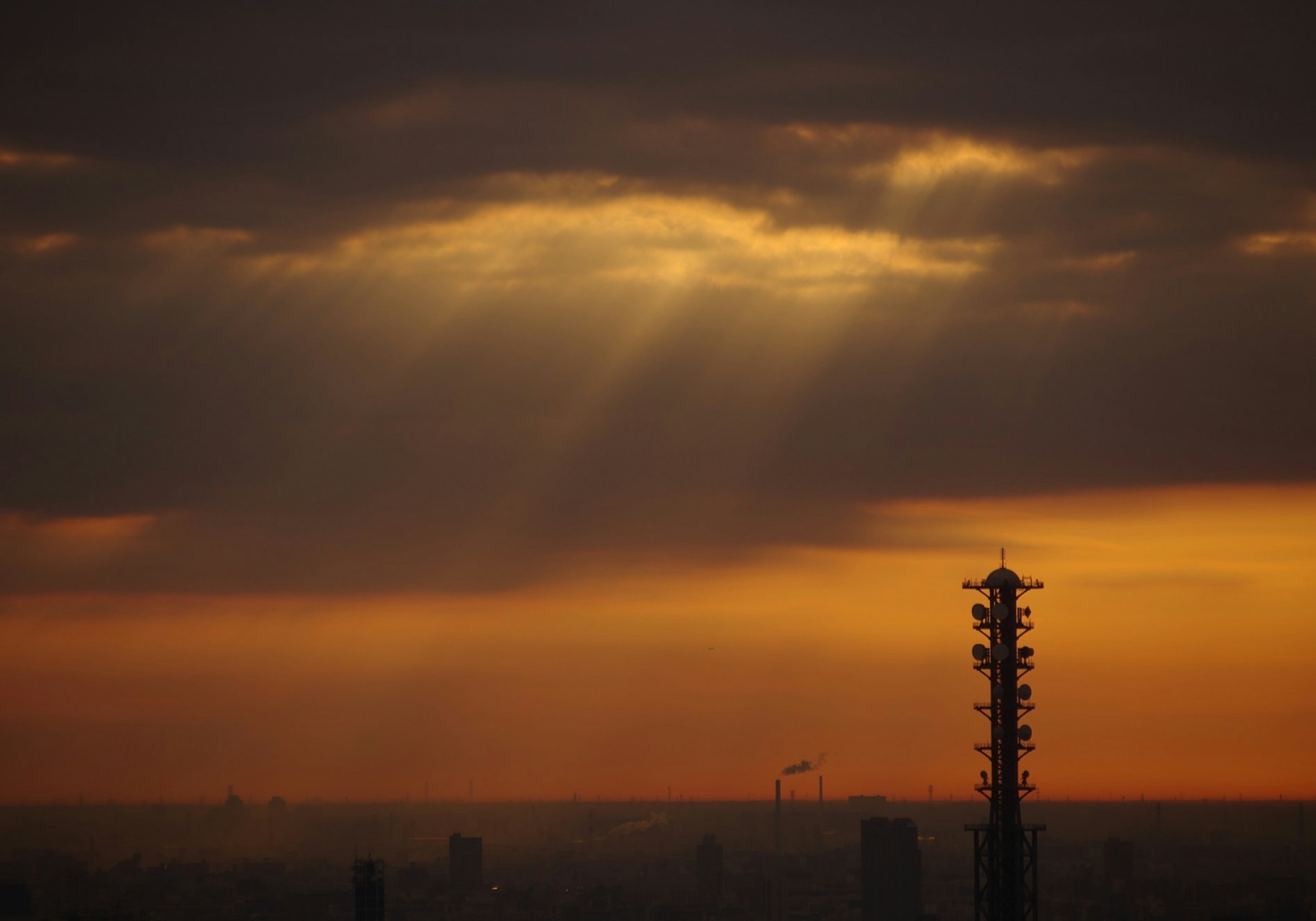 Cielo al tramonto con raggi di luce che attraversano le nuvole torre alta in primo piano