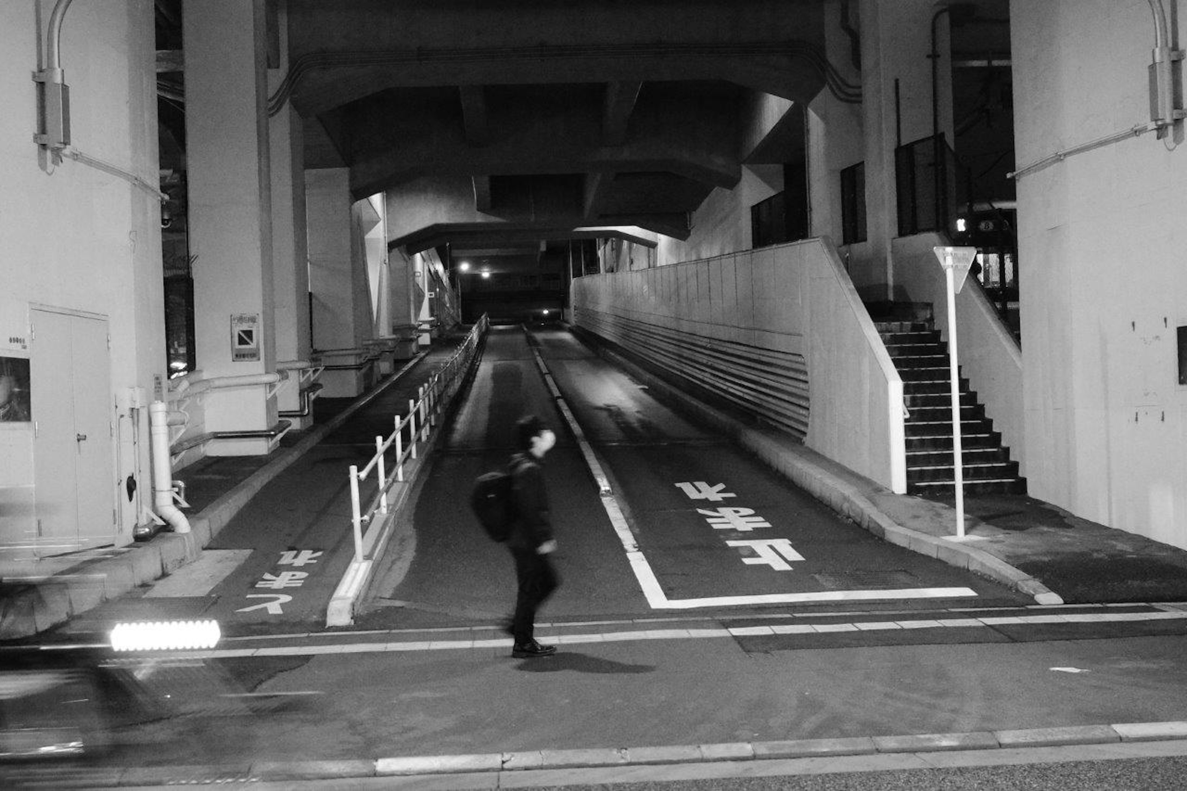 Une silhouette traversant une rue urbaine sombre sous un viaduc