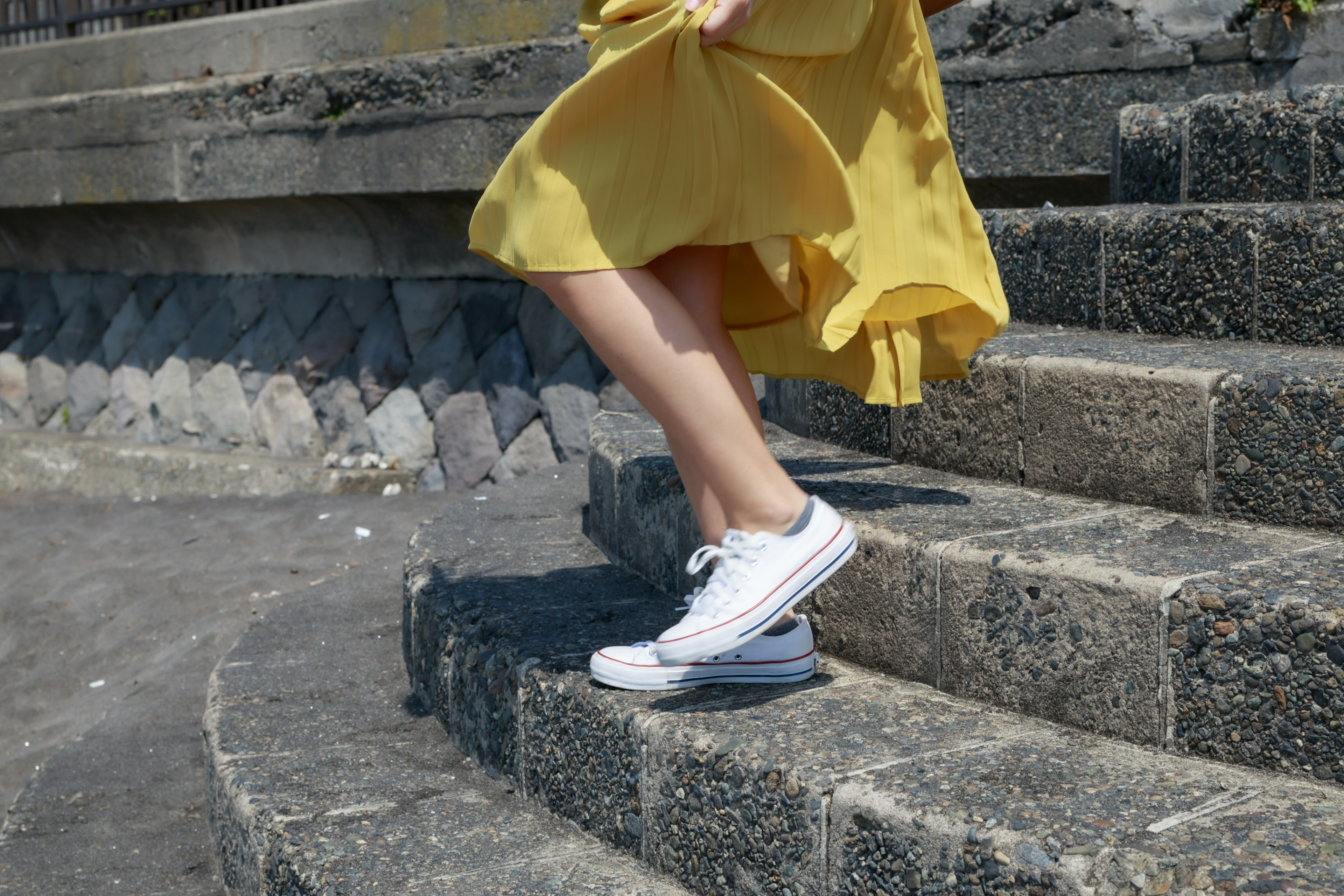 A woman in a yellow dress descending stairs wearing white sneakers