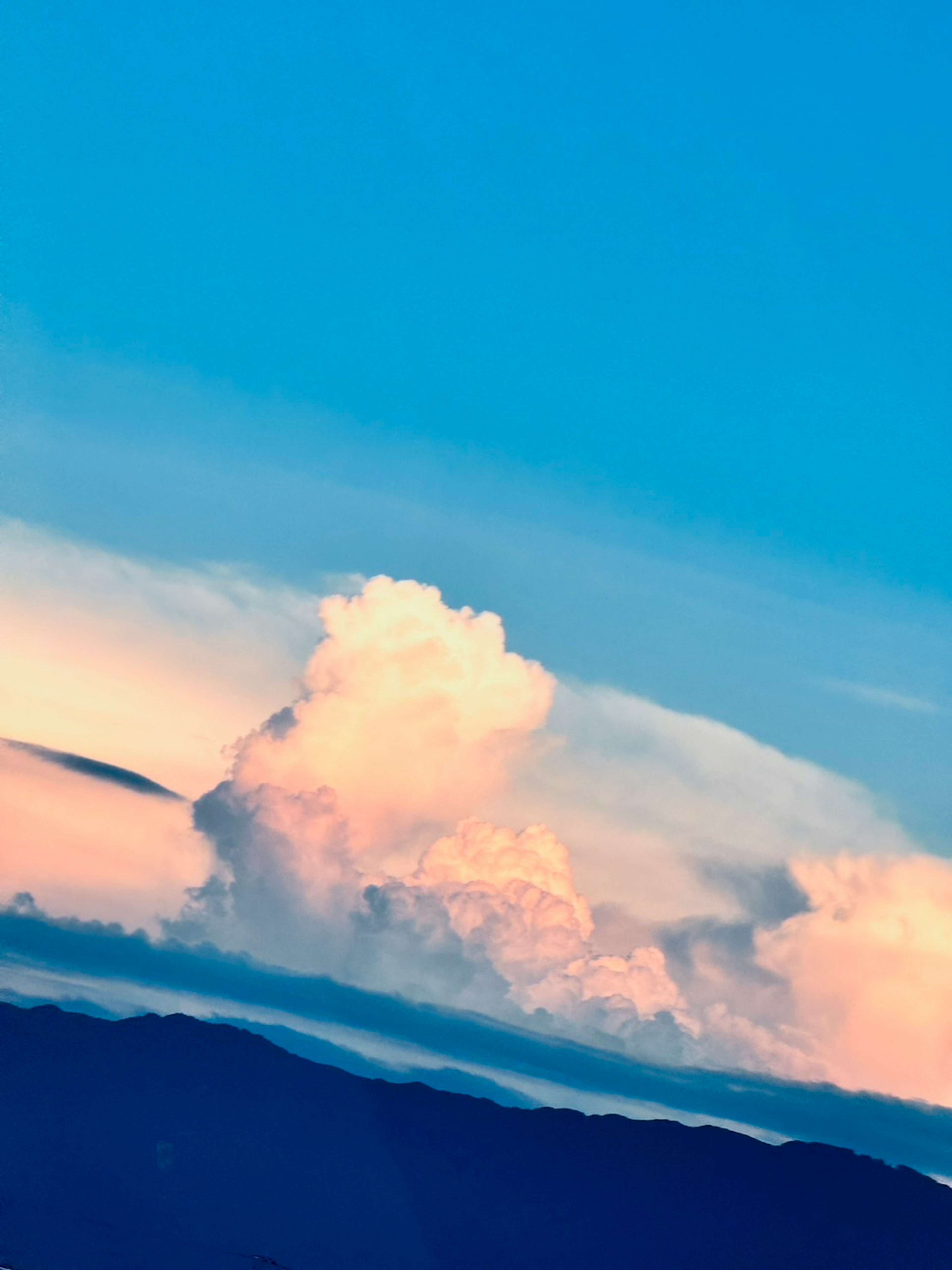 Fluffige weiße Wolken vor blauem Himmel mit Bergsilhouette