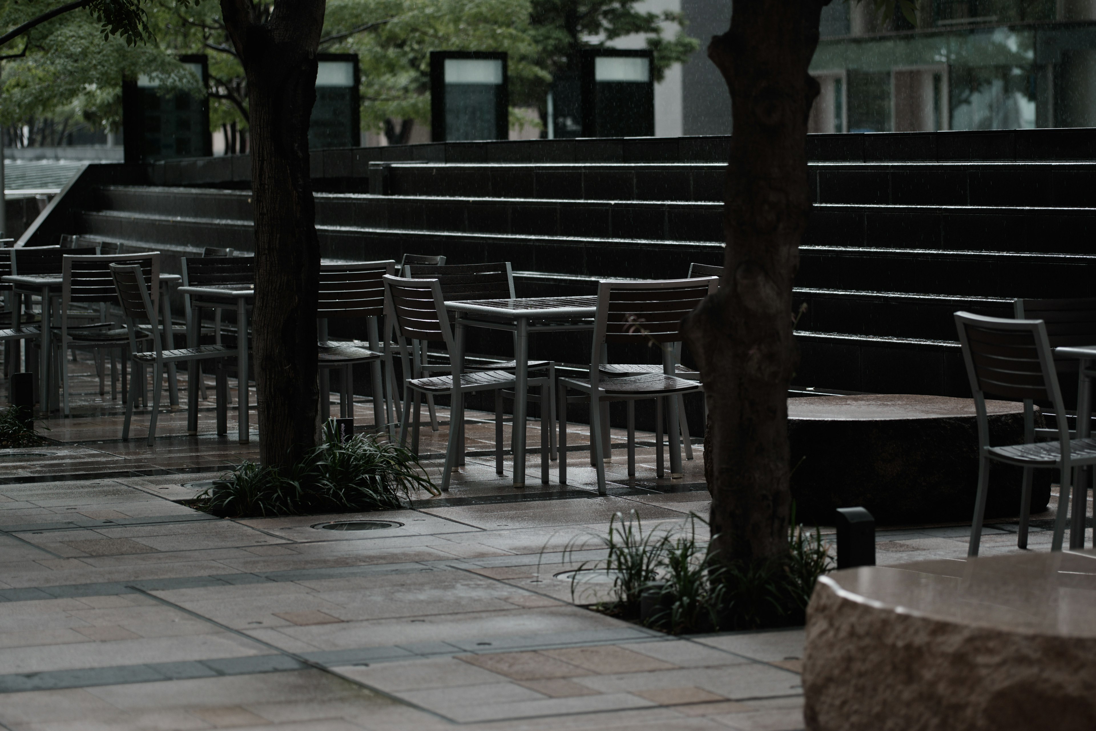 Metal chairs and tables arranged on an outdoor terrace in the rain