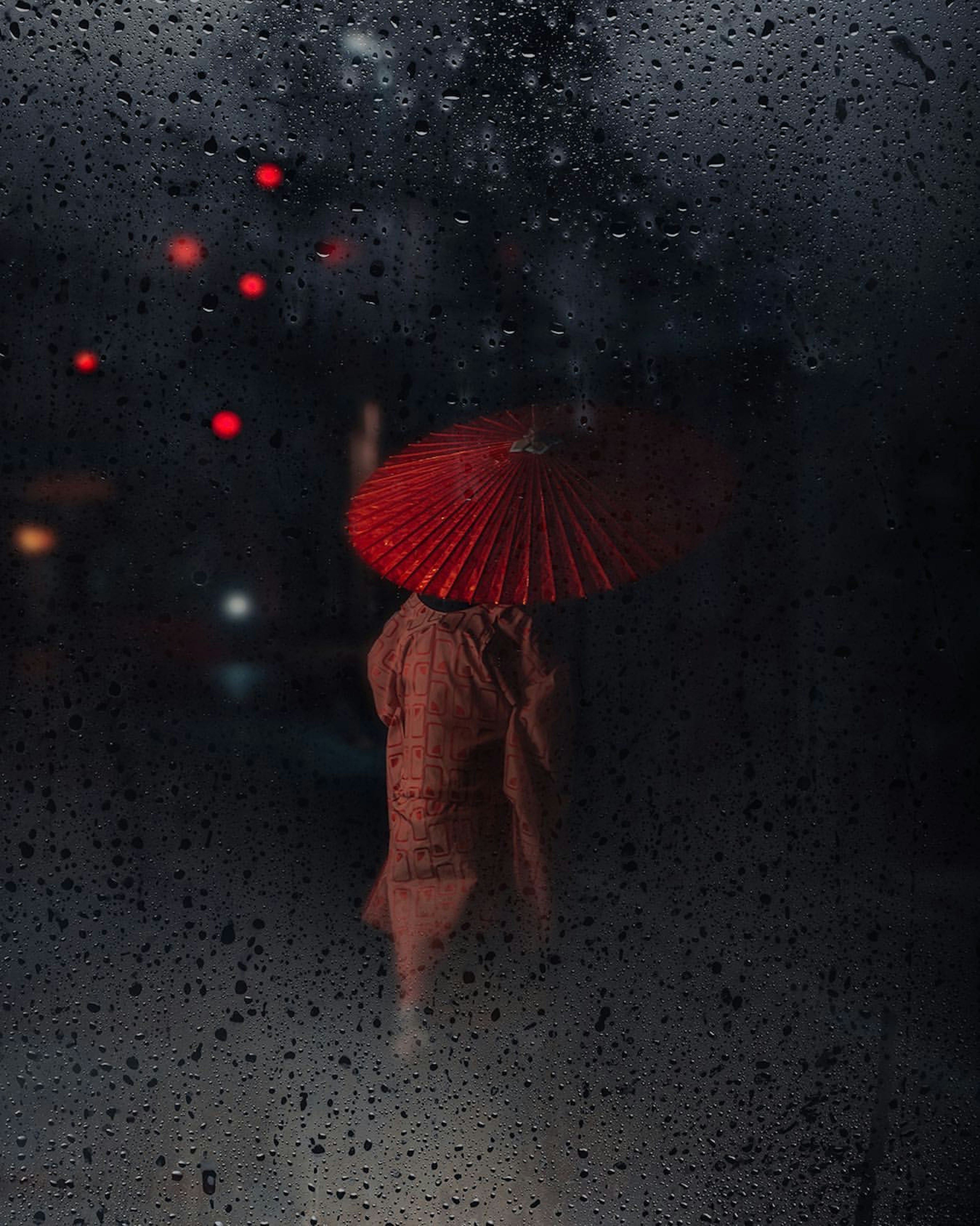 Silhouette einer Person mit einem roten Regenschirm, gesehen durch ein beschlagenes Fenster im Regen