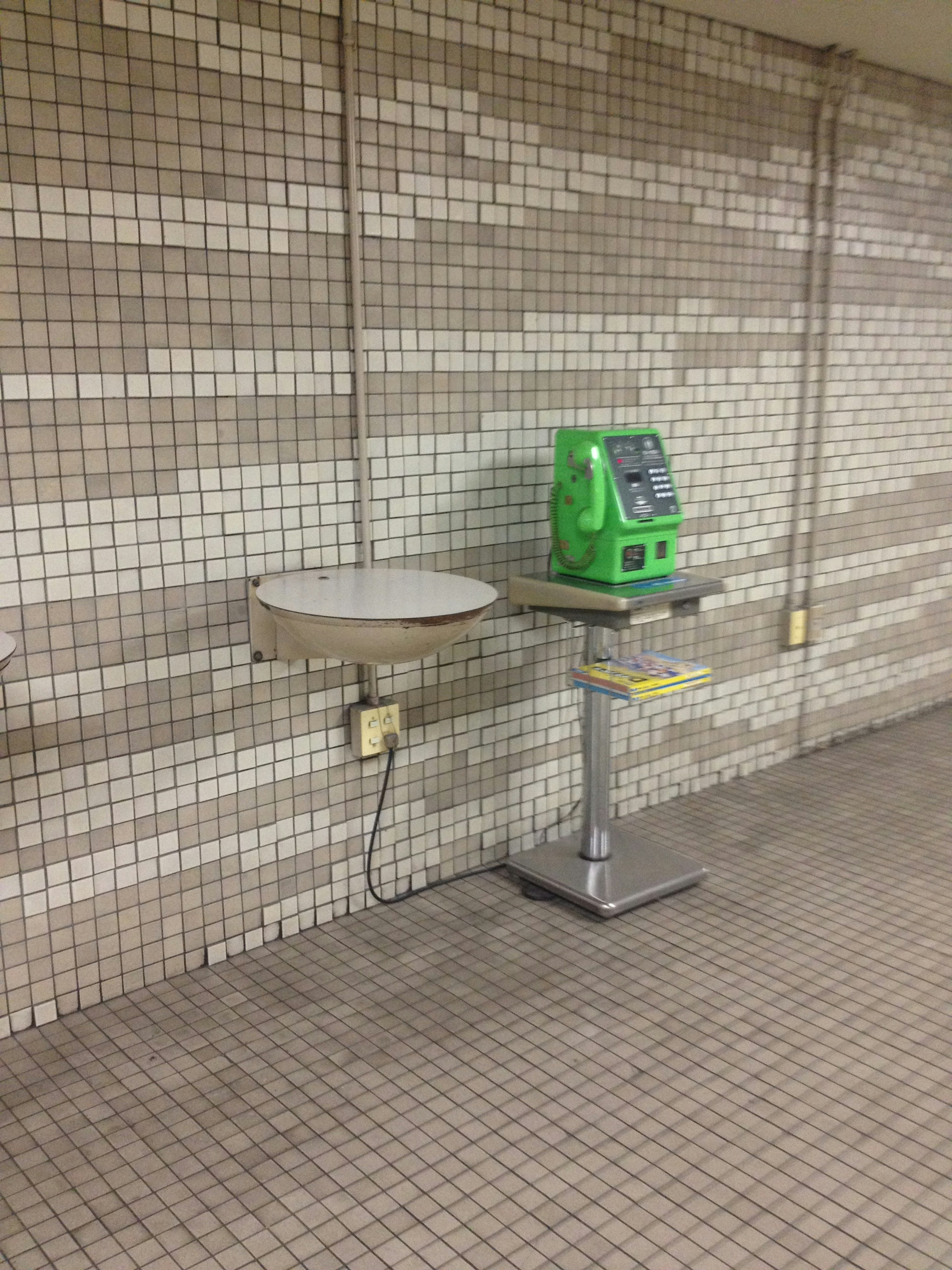 Green machine next to a round table against a tiled wall in a subway station