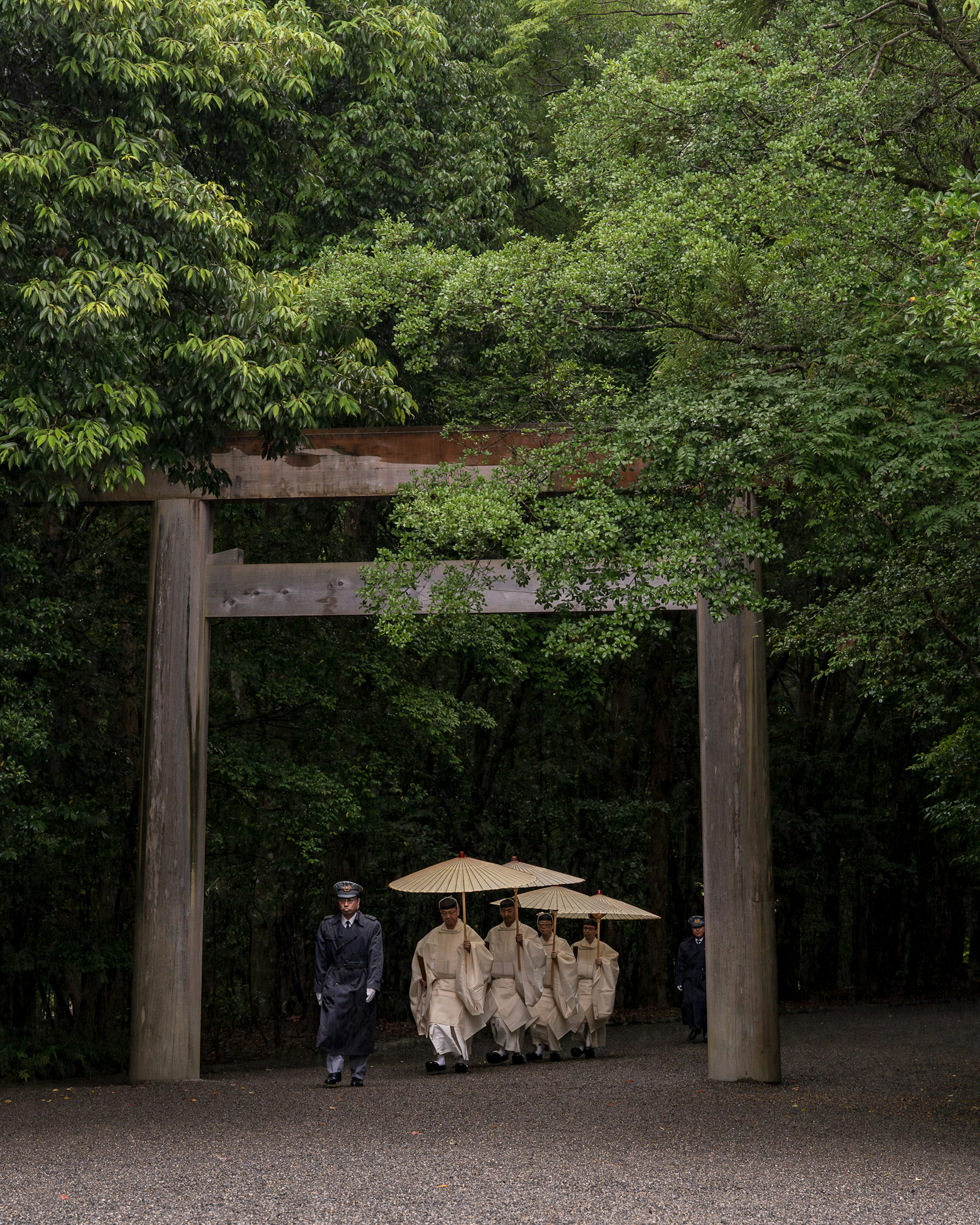 Personas vestidas tradicionalmente caminando bajo una puerta torii rodeada de vegetación exuberante