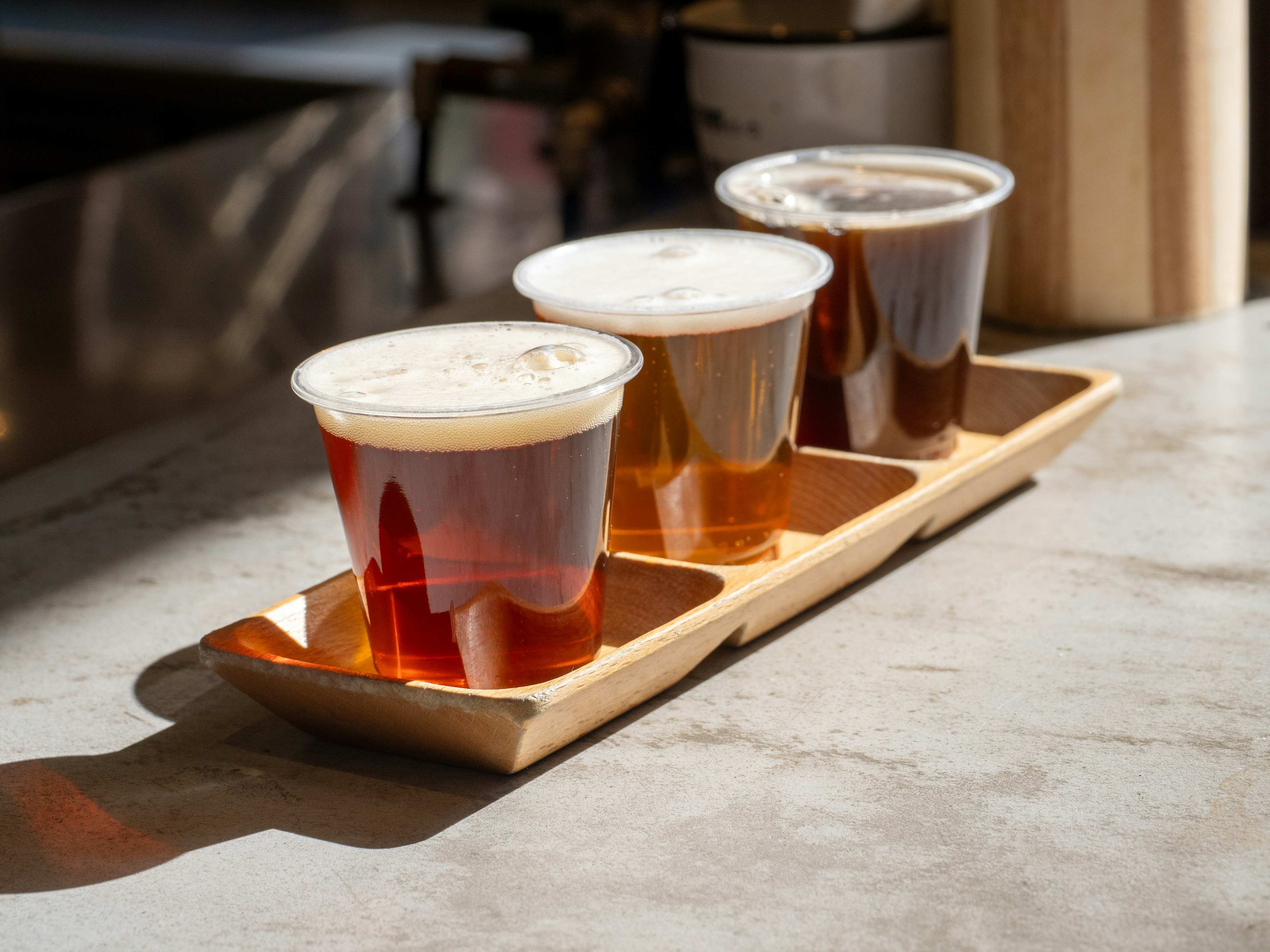 Three cups of beer arranged on a wooden tray