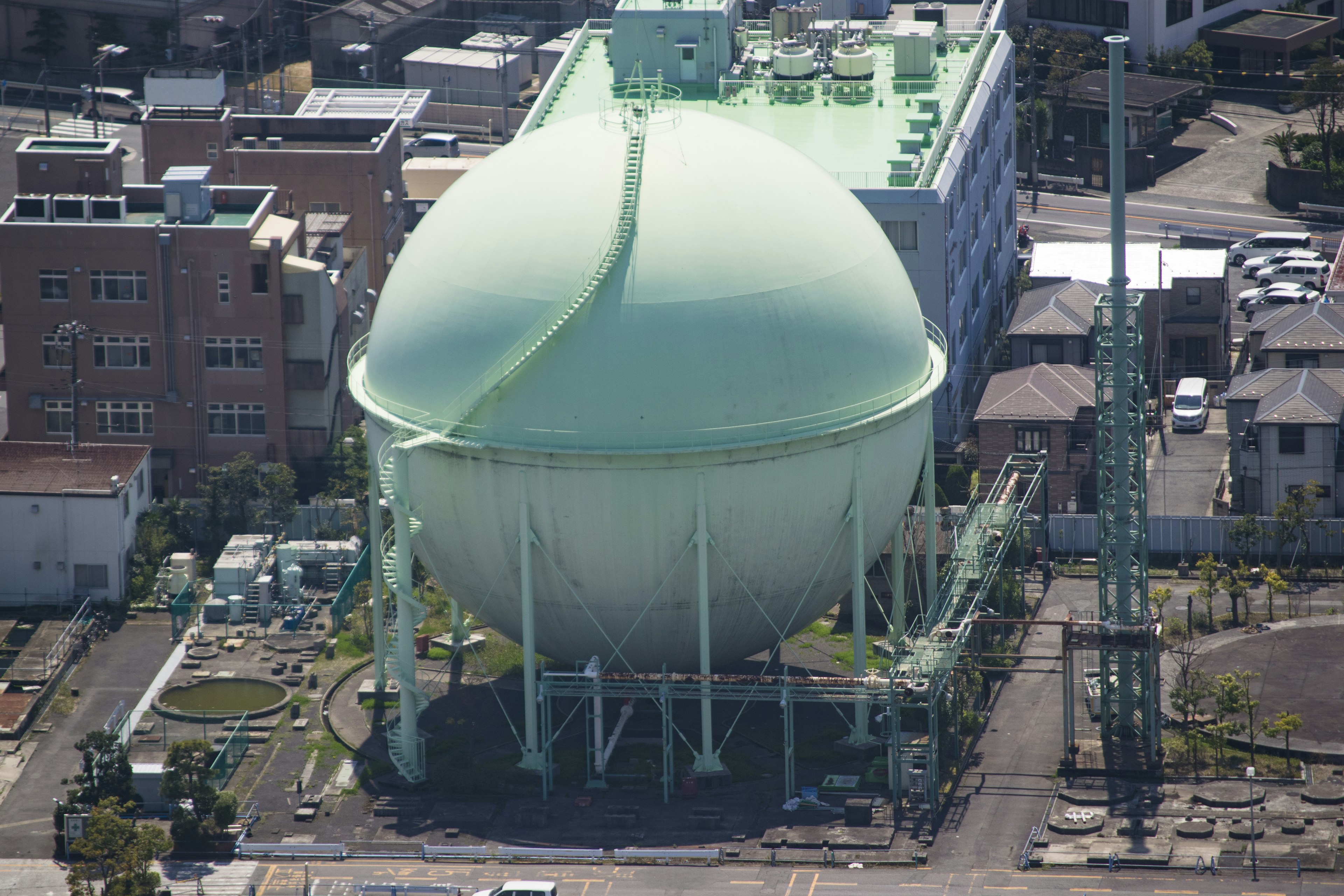 Gran tanque esférico verde situado cerca de edificios industriales