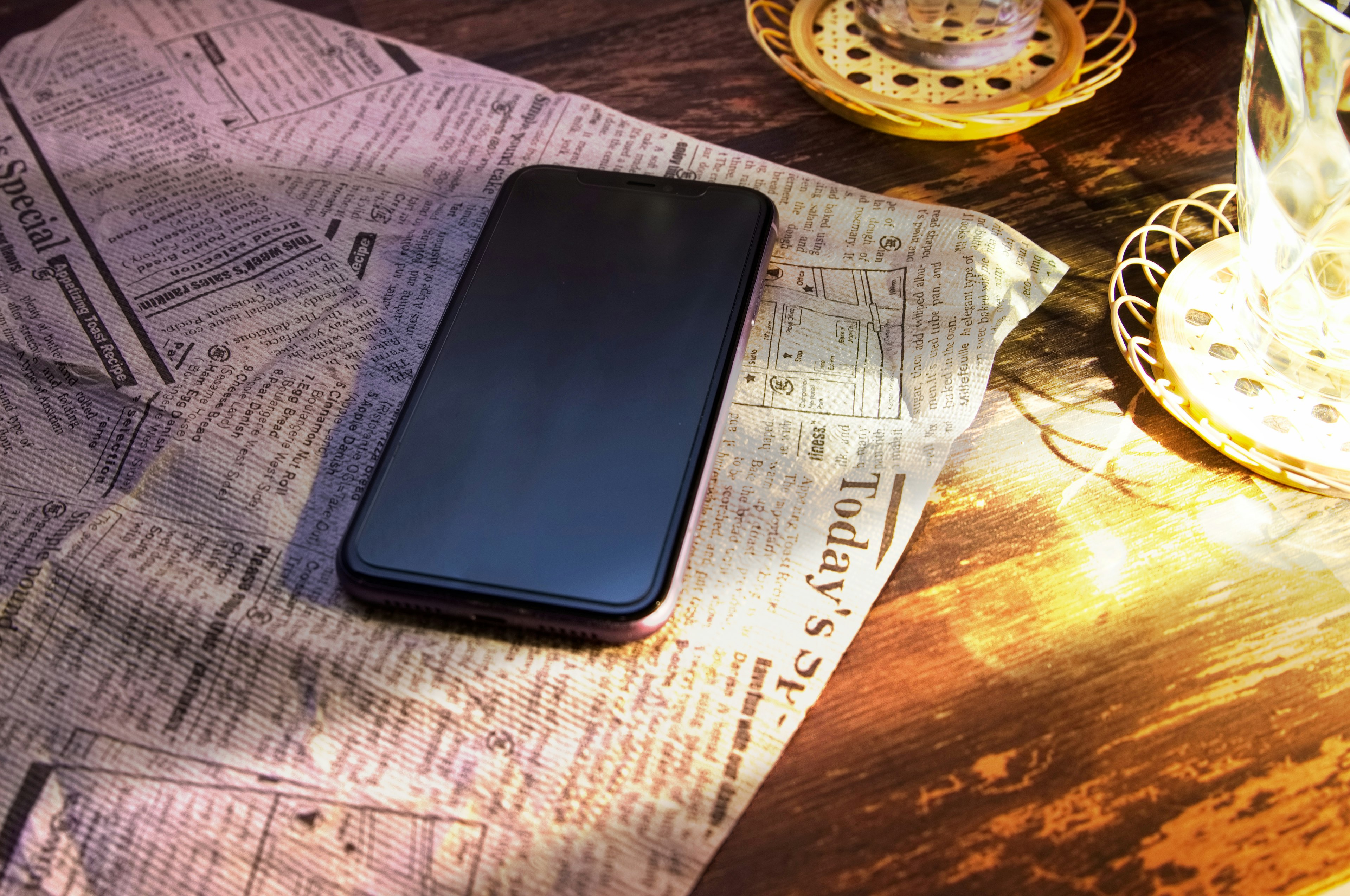 A smartphone on a newspaper spread across a wooden table