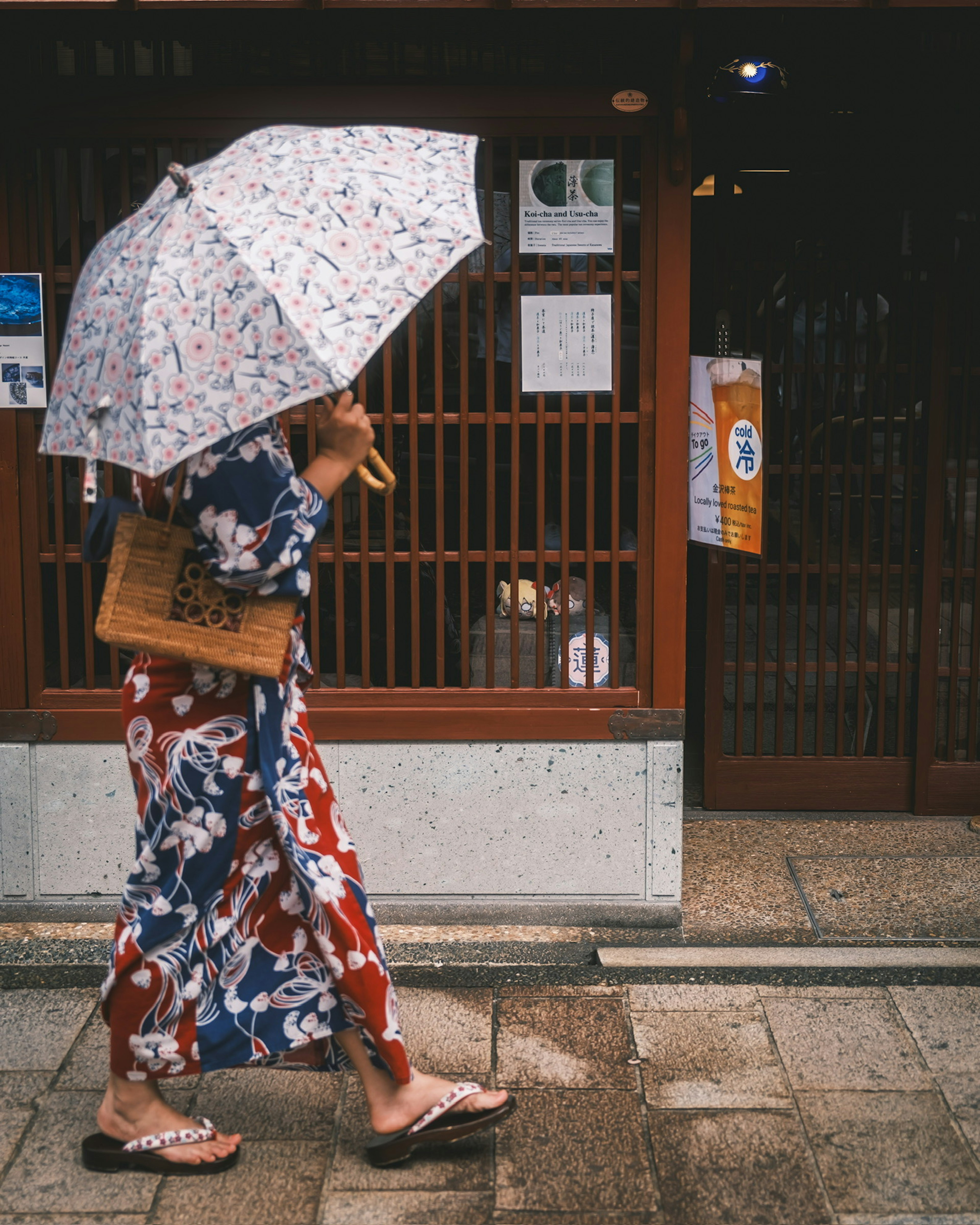 Seorang wanita berpakaian kimono berjalan di jalan sambil memegang payung