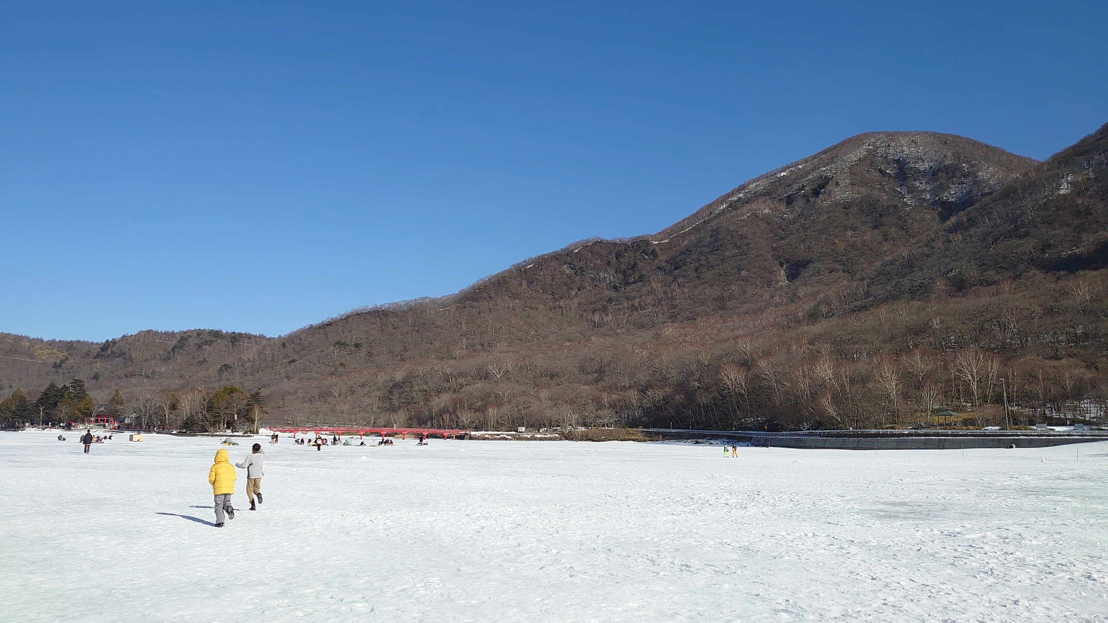 Persone che camminano sul ghiaccio sotto un cielo blu chiaro con montagne sullo sfondo