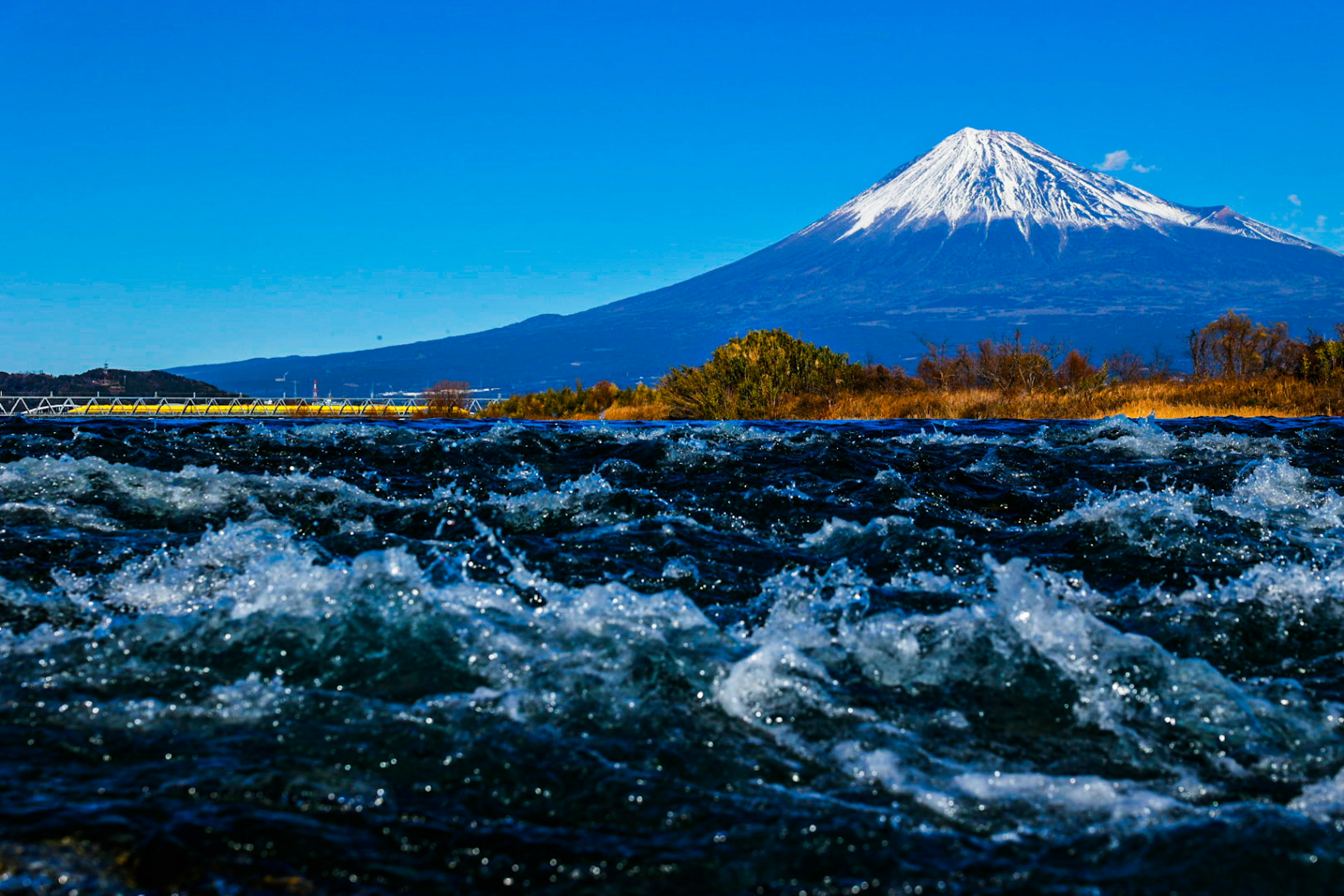 Air sungai yang memercik dengan Gunung Fuji di latar belakang di bawah langit biru cerah