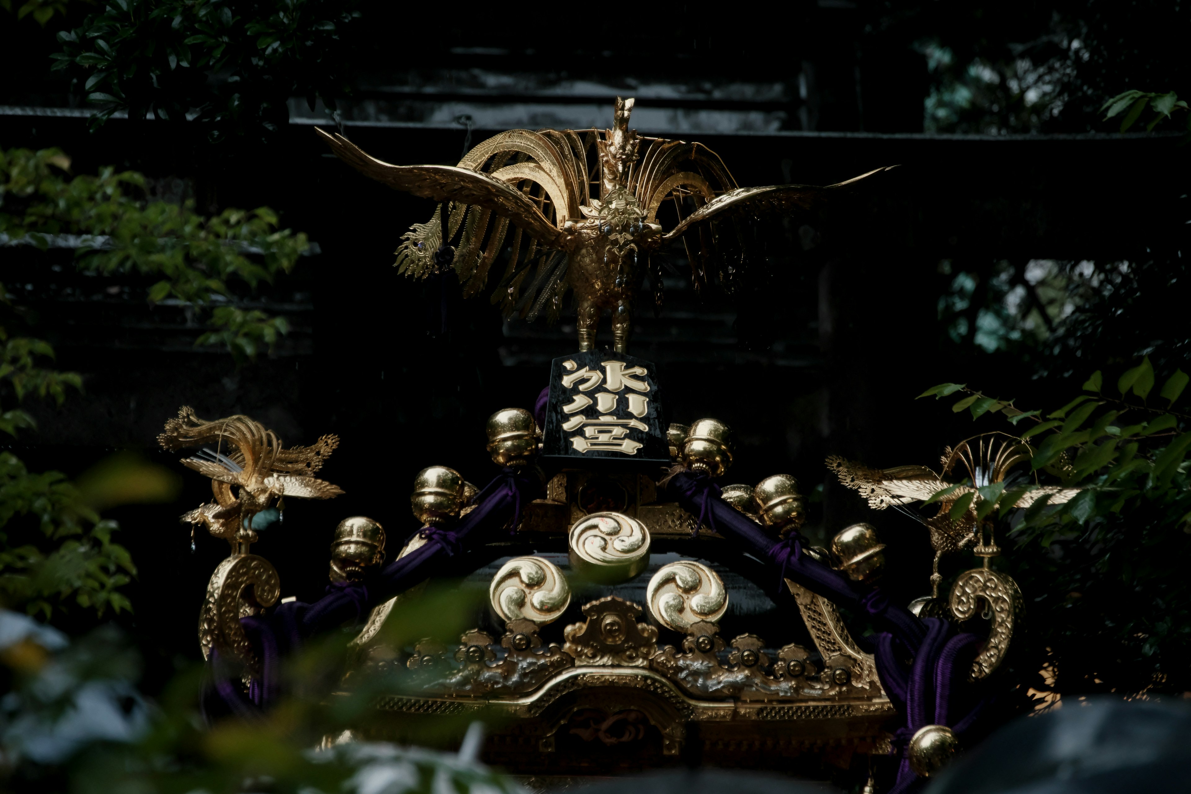 Una sección de un mikoshi de santuario adornada con decoraciones doradas que presenta una escultura de grúa majestuosa y tela morada