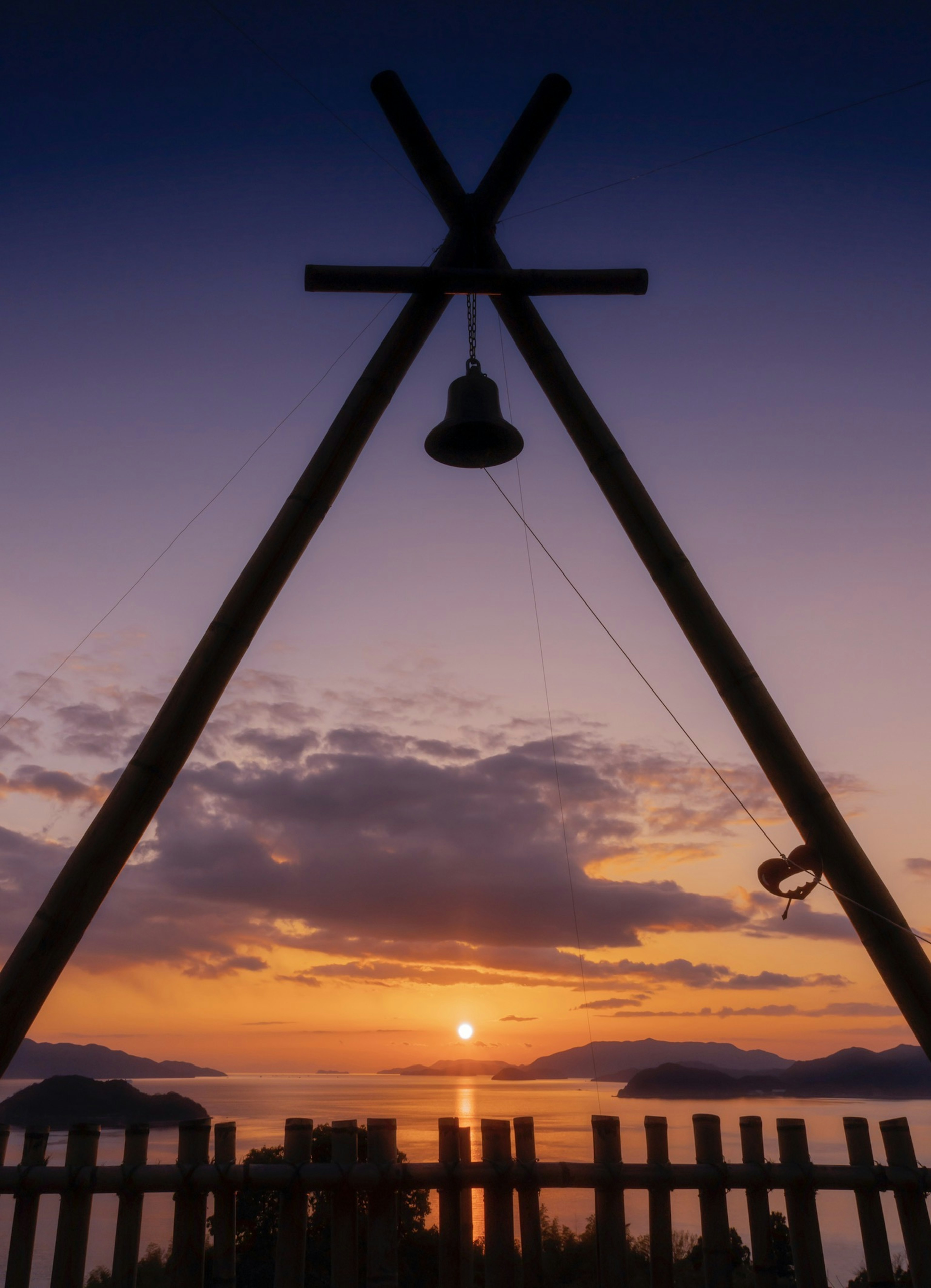 Wooden structure with a bell silhouetted against a sunset