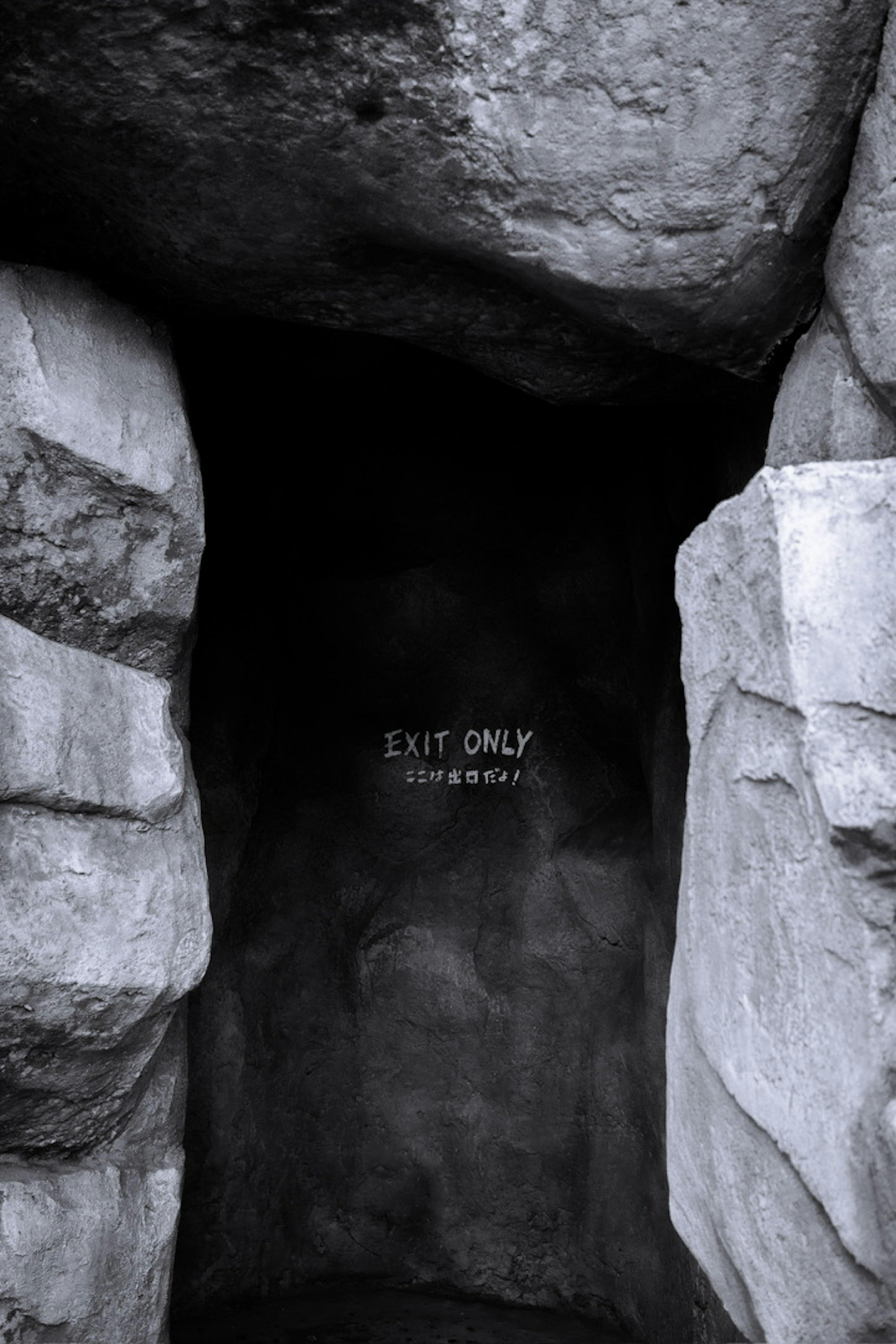 Entrance of a tunnel in black and white surrounded by rocks with an exit only sign