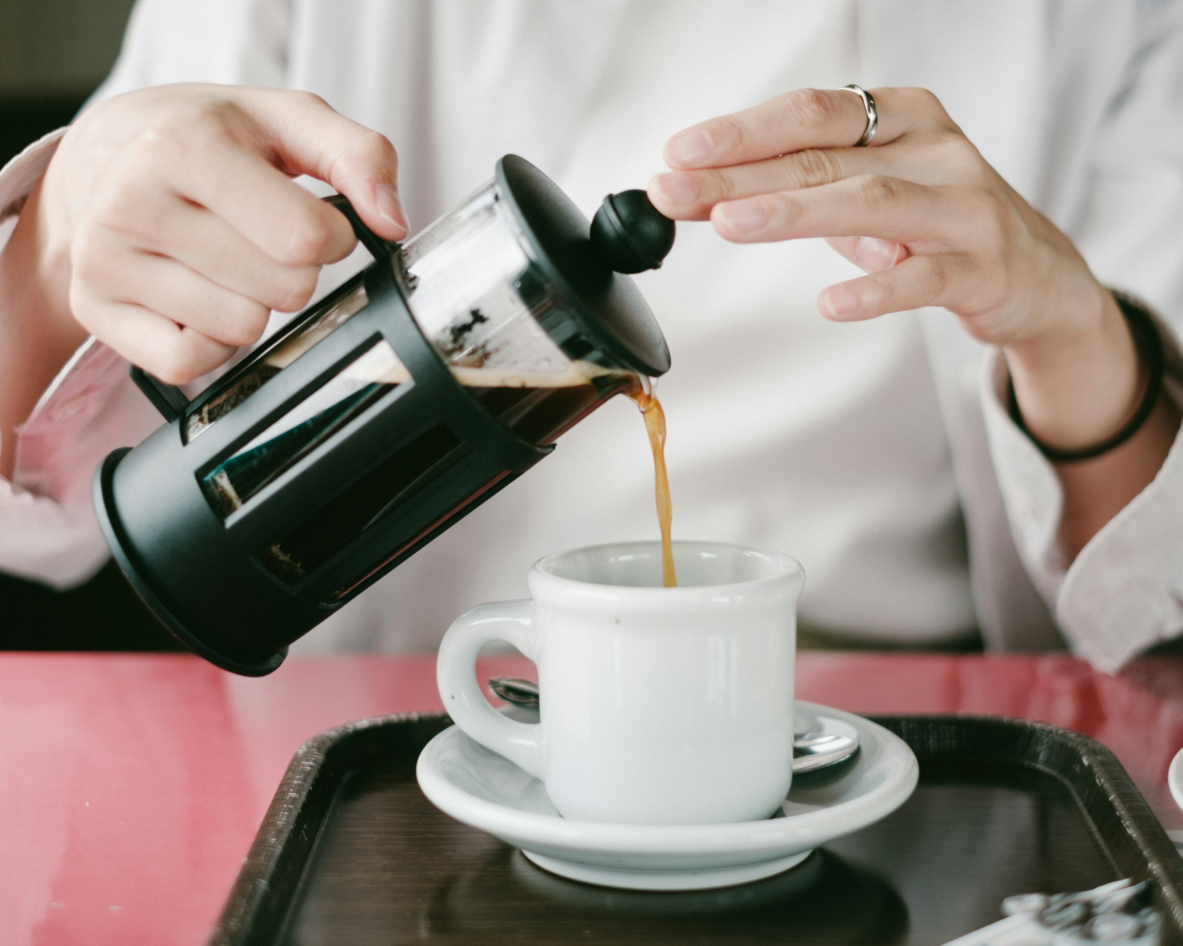 Gros plan sur des mains versant du café d'une cafetière à piston dans une tasse blanche