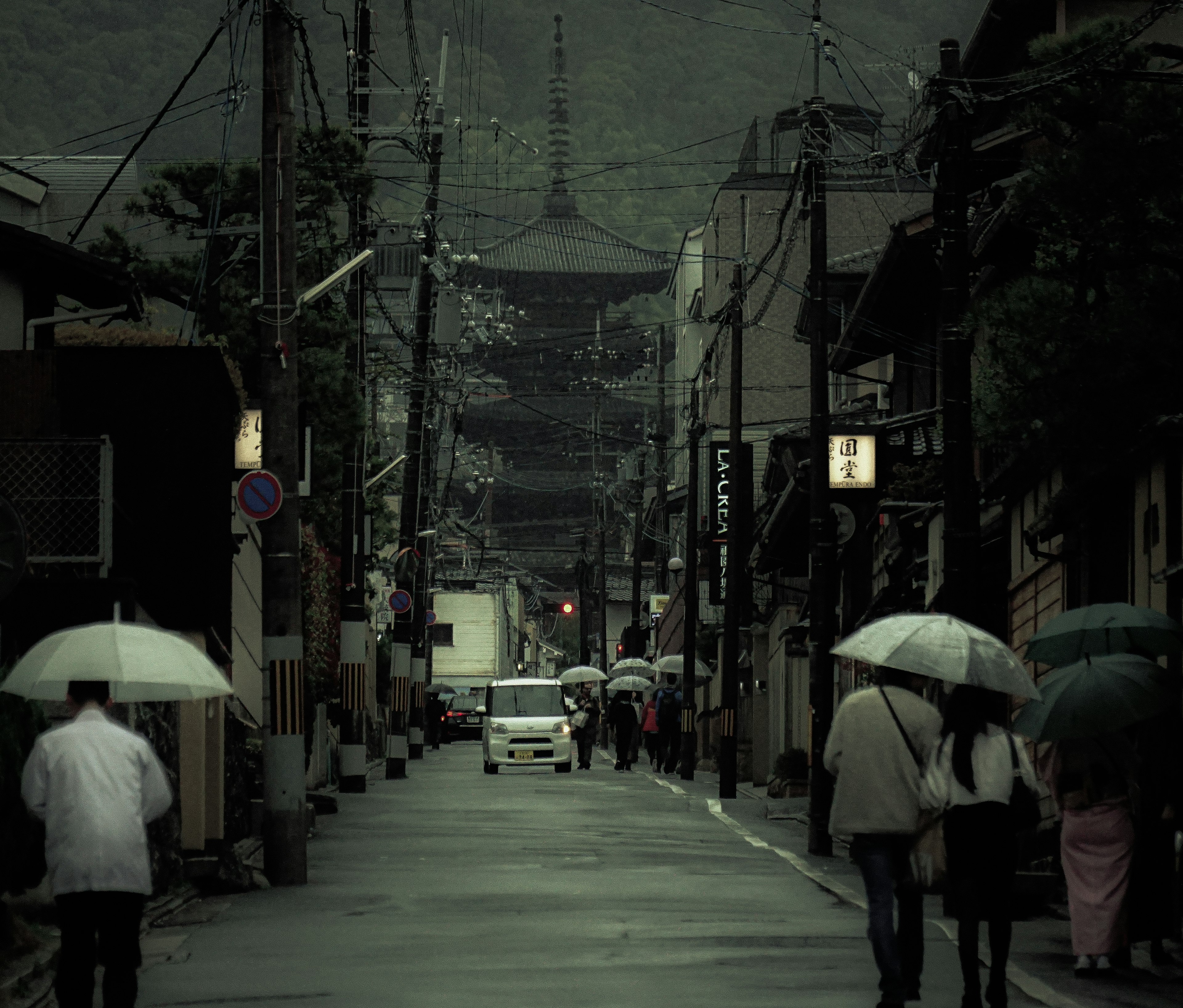 雨の中、傘を持った人々が並ぶ静かな街並みと寺の背景