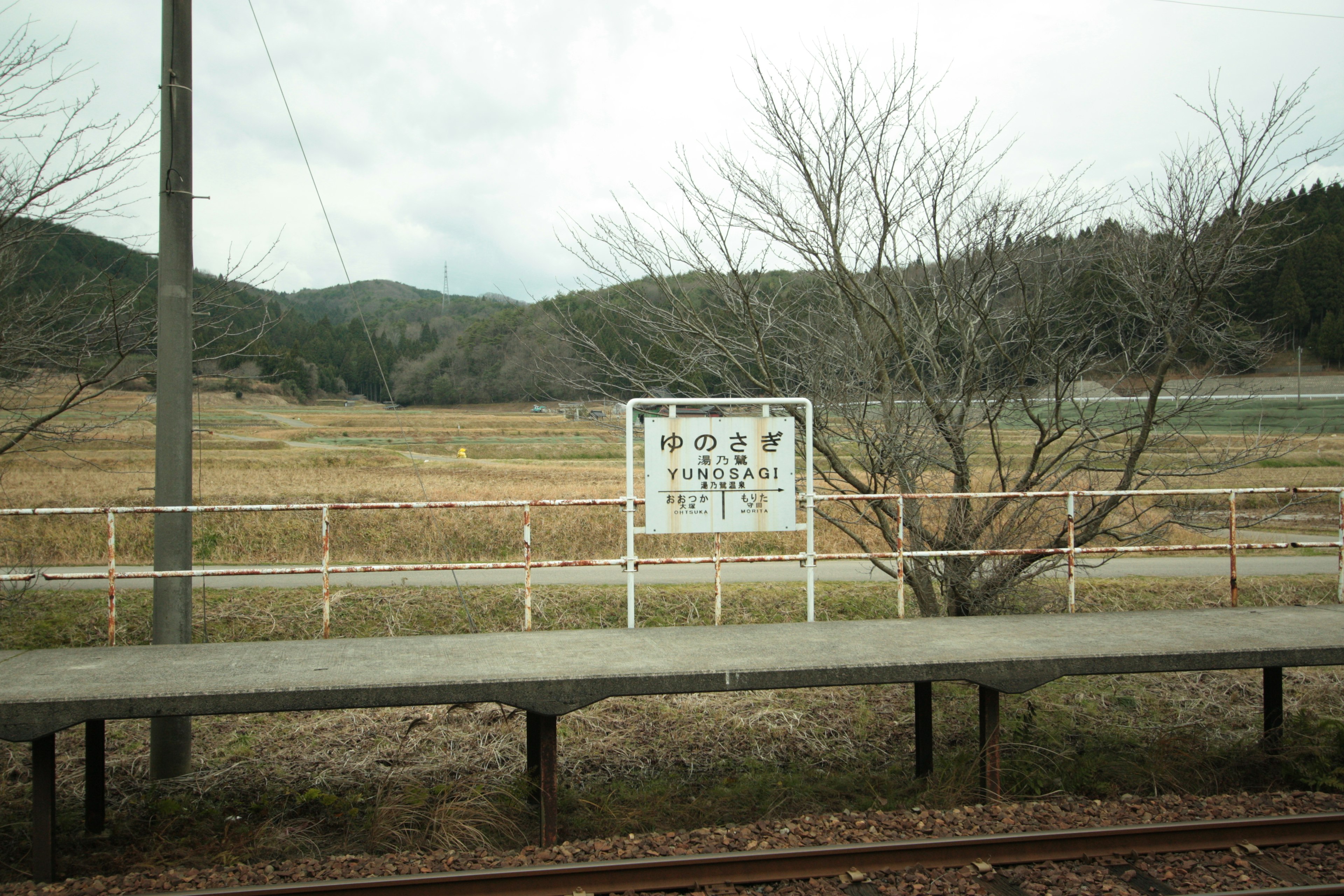 Rural train station platform with a sign and surrounding landscape