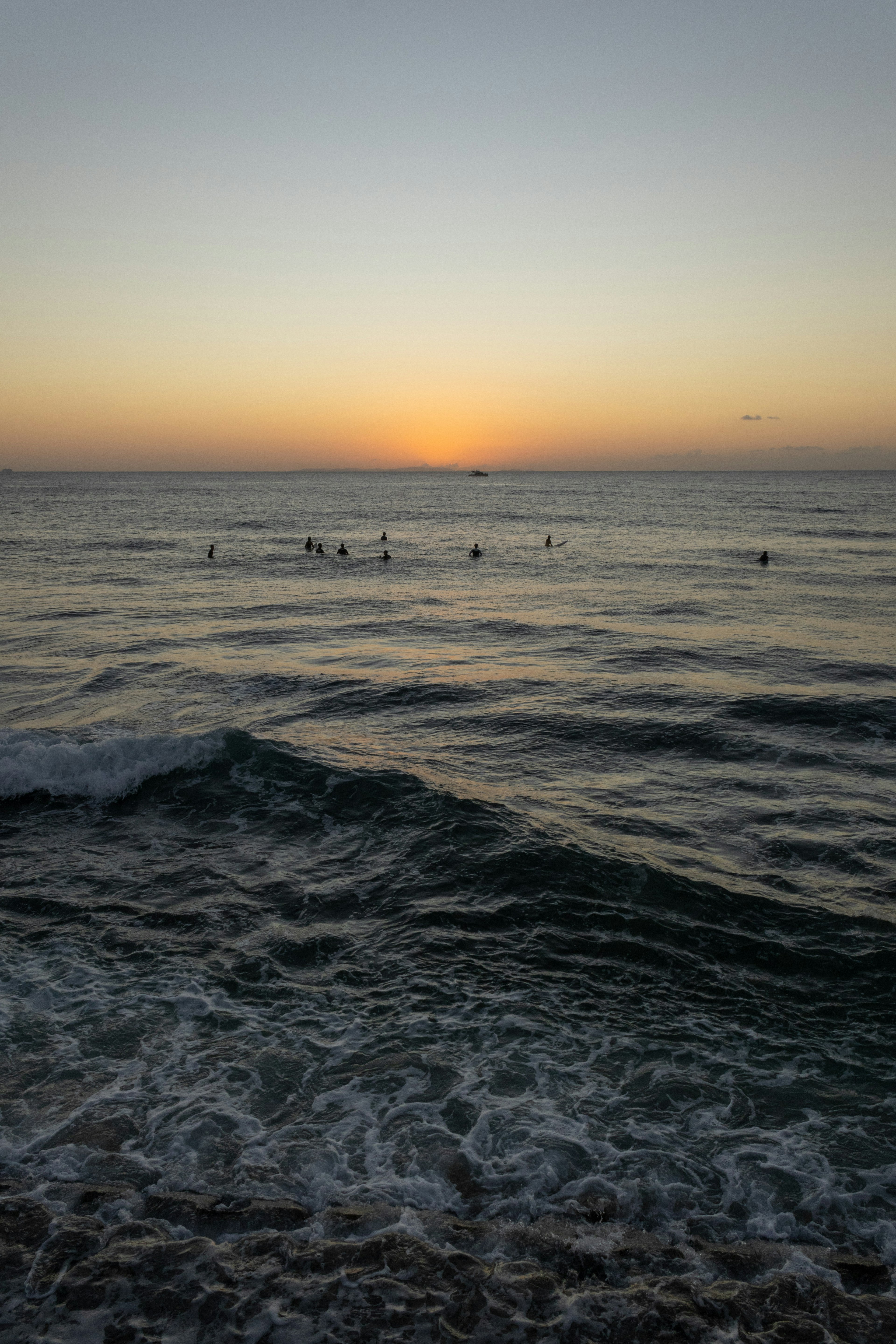 Silhouetten von Menschen, die im Ozean bei Sonnenuntergang surfen