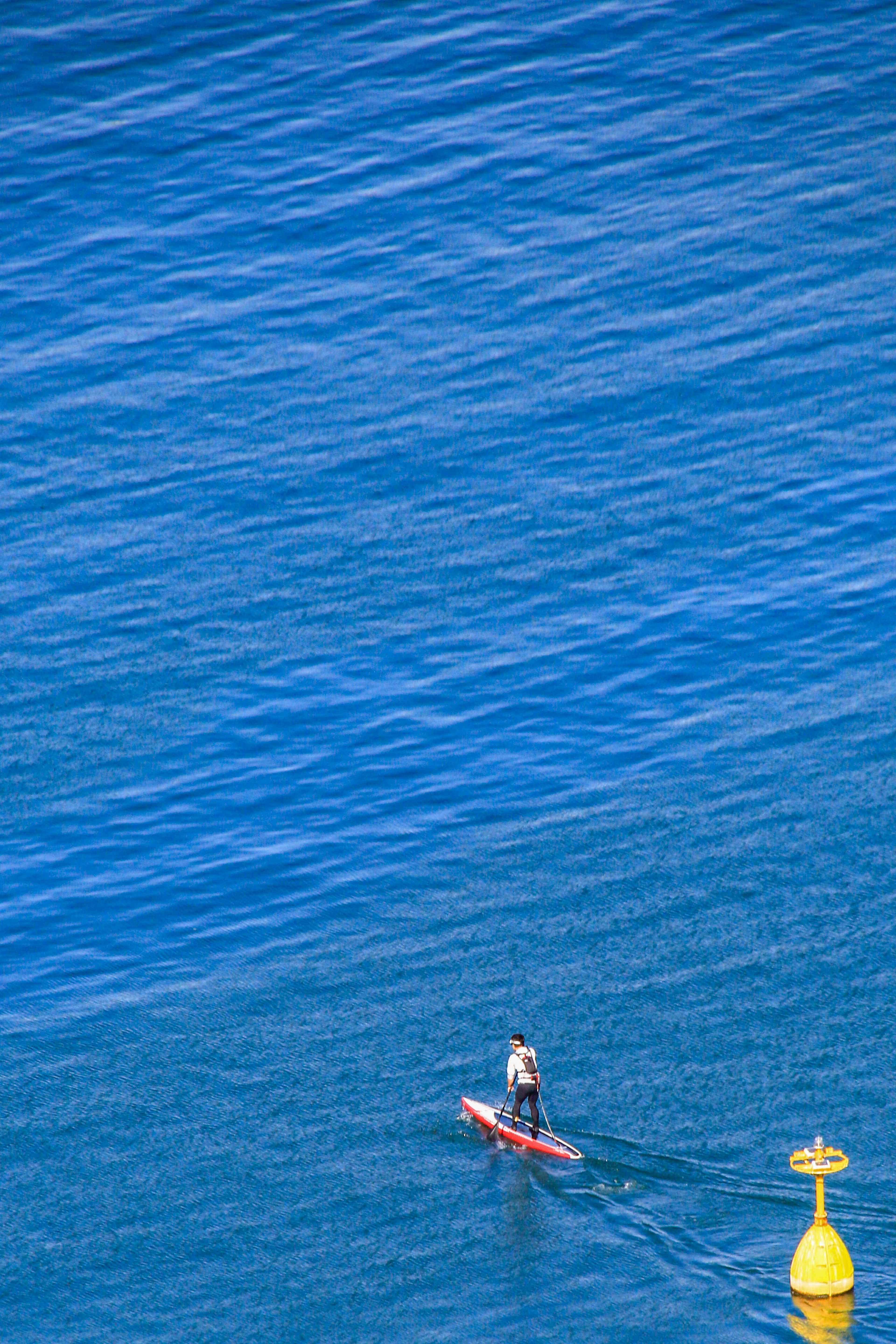 A kayaker paddling on a blue ocean with a yellow buoy nearby