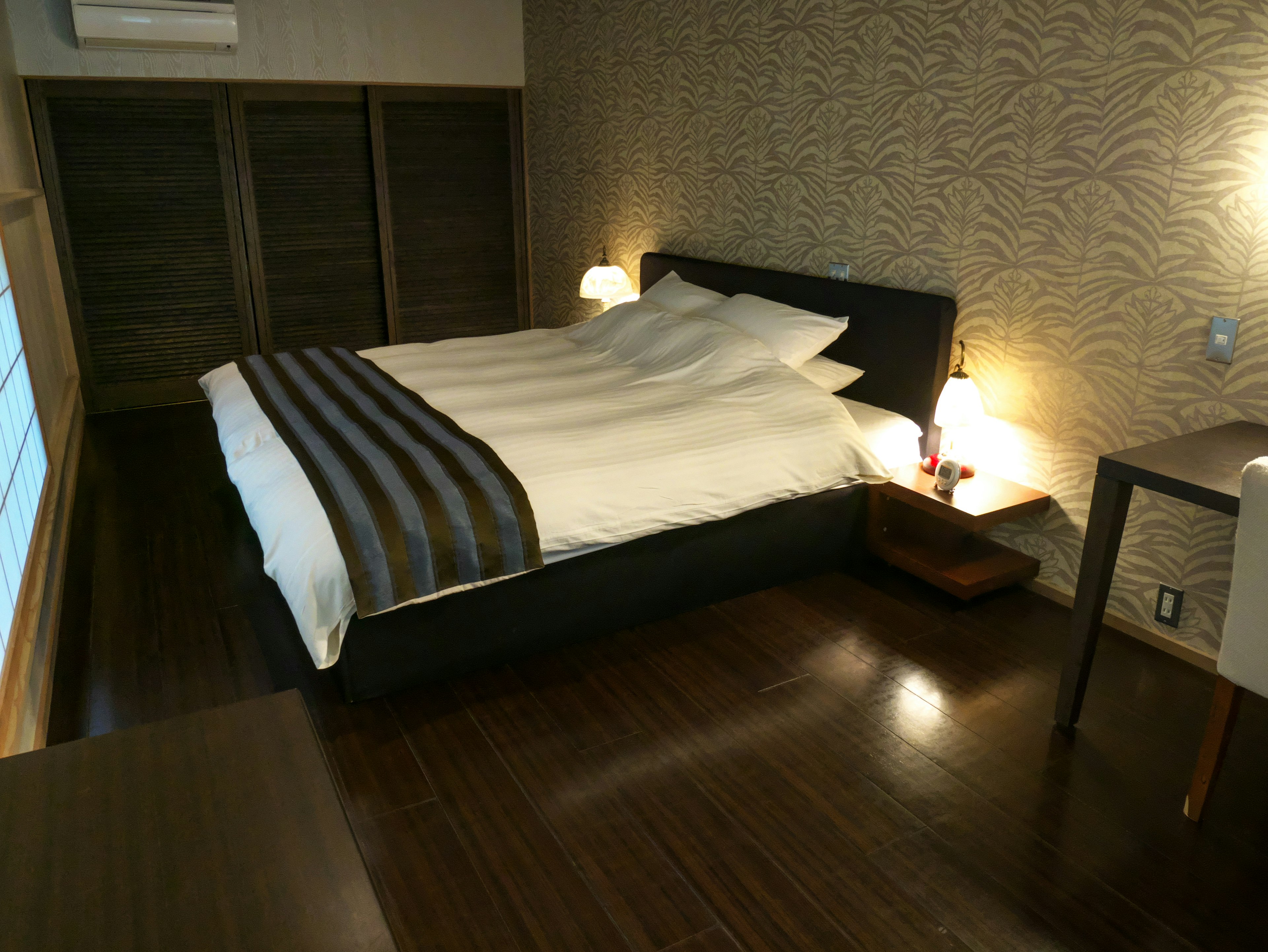 Modern bedroom design with a simple bed and dark wood flooring featuring natural lighting